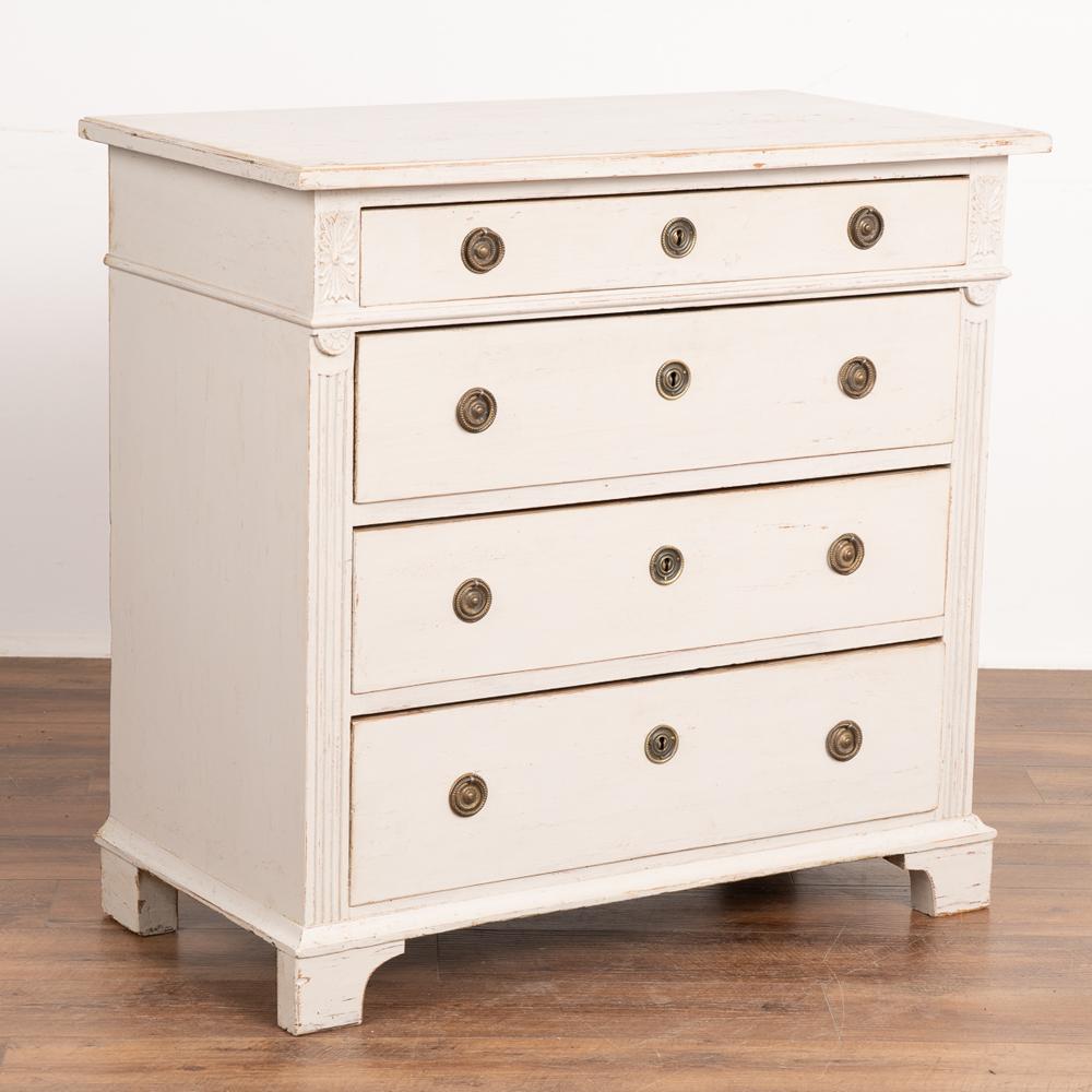 Antique pine chest of four drawers, with traditional fluted carved details along side and topped by carved accent medallions flanking the narrow top drawer.
The professionally applied newer white painted finish adds new life to this pine dresser