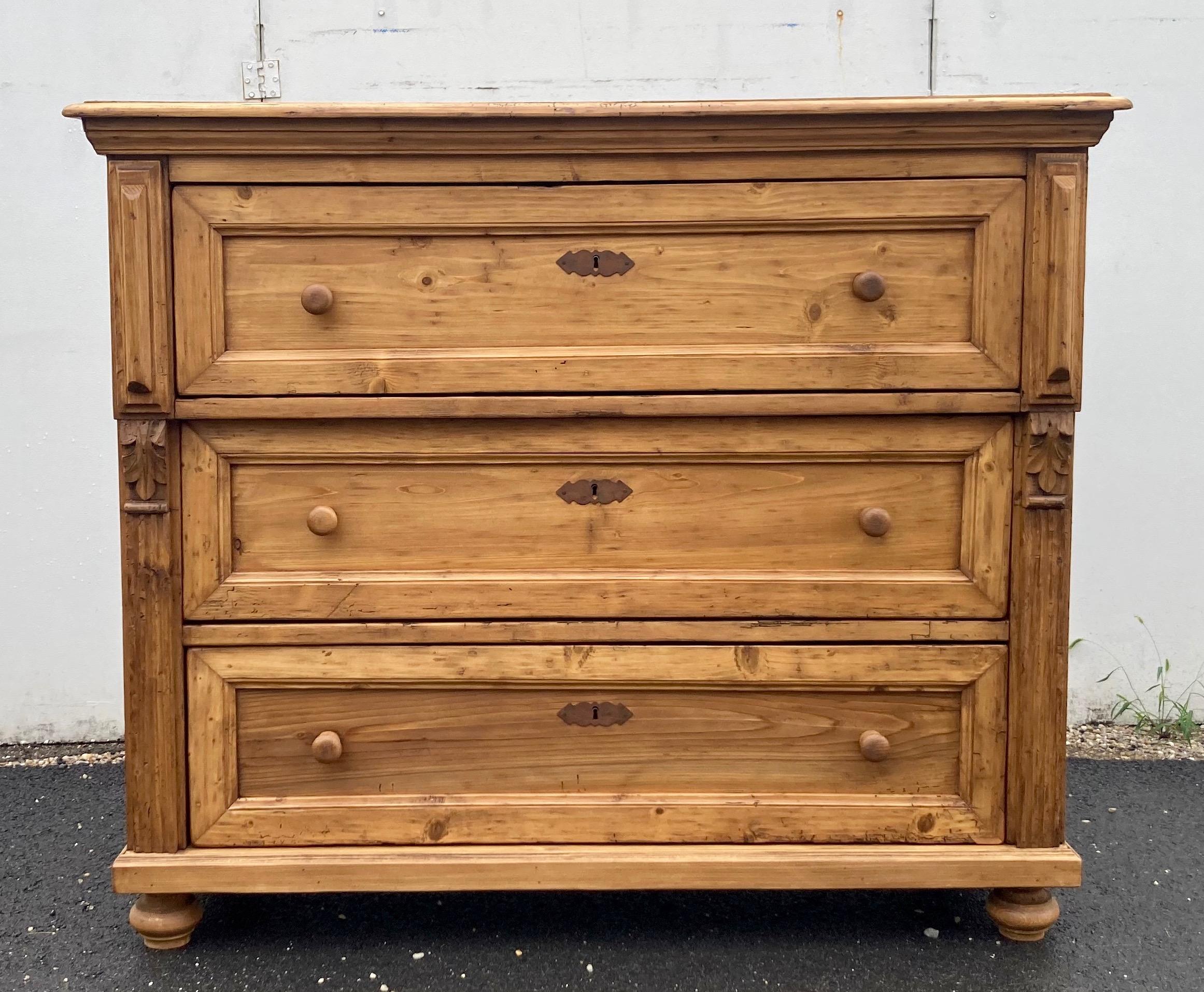 This chest of three hand-cut dovetailed drawers has a step-down edge to the top and a bold ogee crown.  The top drawer stands slightly proud with elongated pyramid appliqués on each side. The lower two are flanked by a broad flute and hand-carved