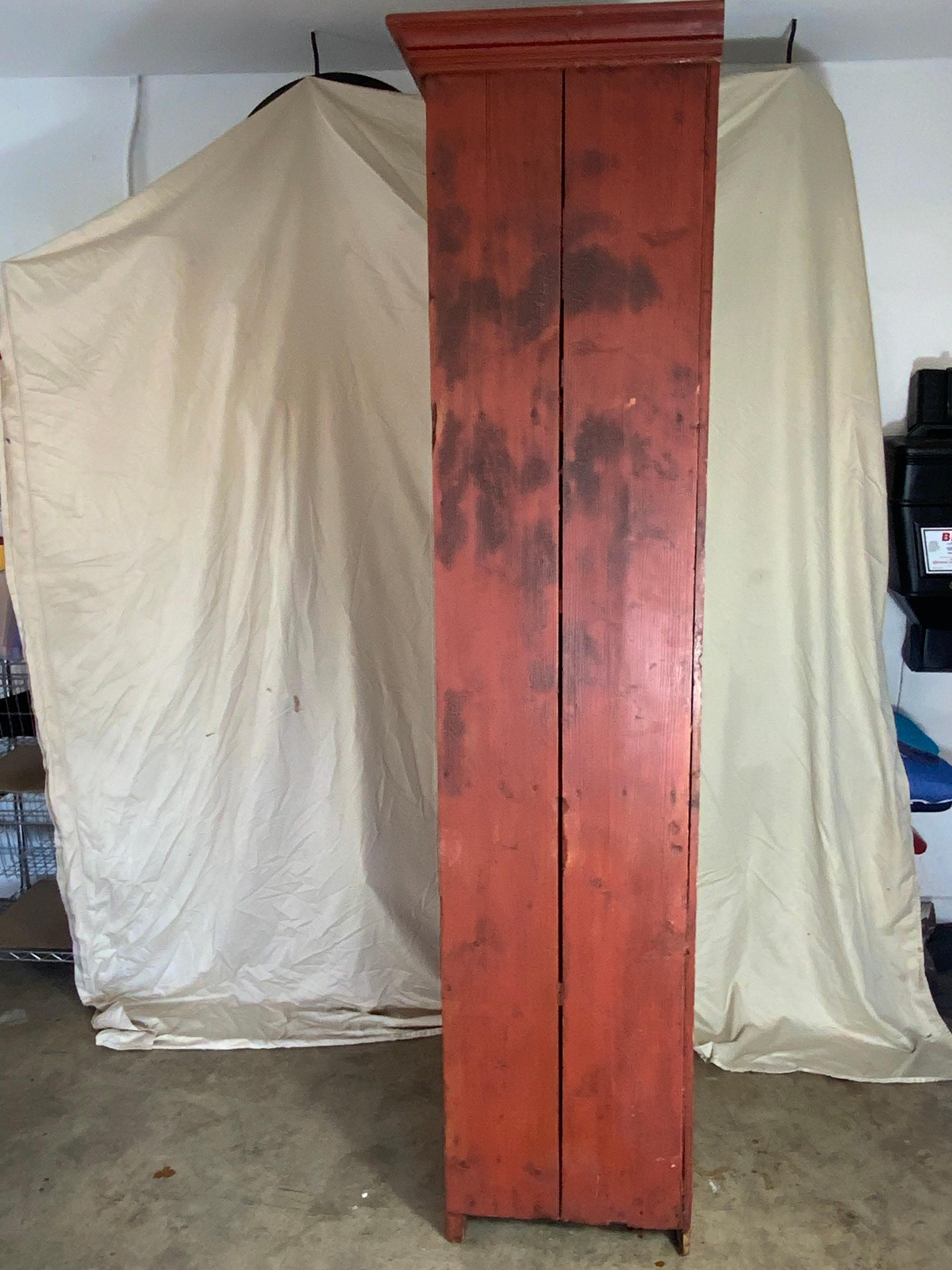 Bonito armario de chimenea primitivo de pino del siglo XIX, de dos puertas, con pintura roja antigua sobre el color salmón original.  Construcción con juntas de mortaja y espiga en las puertas y estantes extraíbles en la parte superior e inferior.