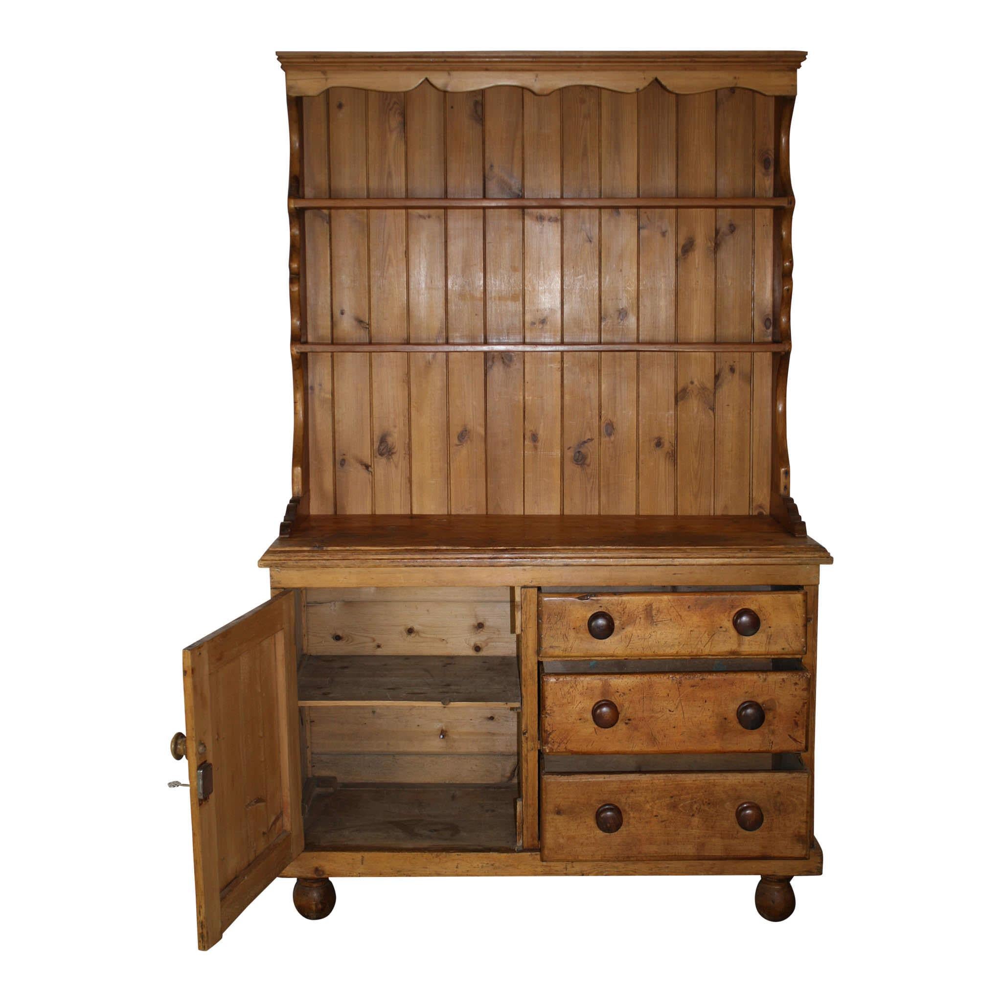 Comprised of two plate rack shelves, three drawers, and a door that opens to a single shelf, this charming pine cupboard provides practical storage and a set back display. The upper piece, which can be removed from the lower piece, is framed with a