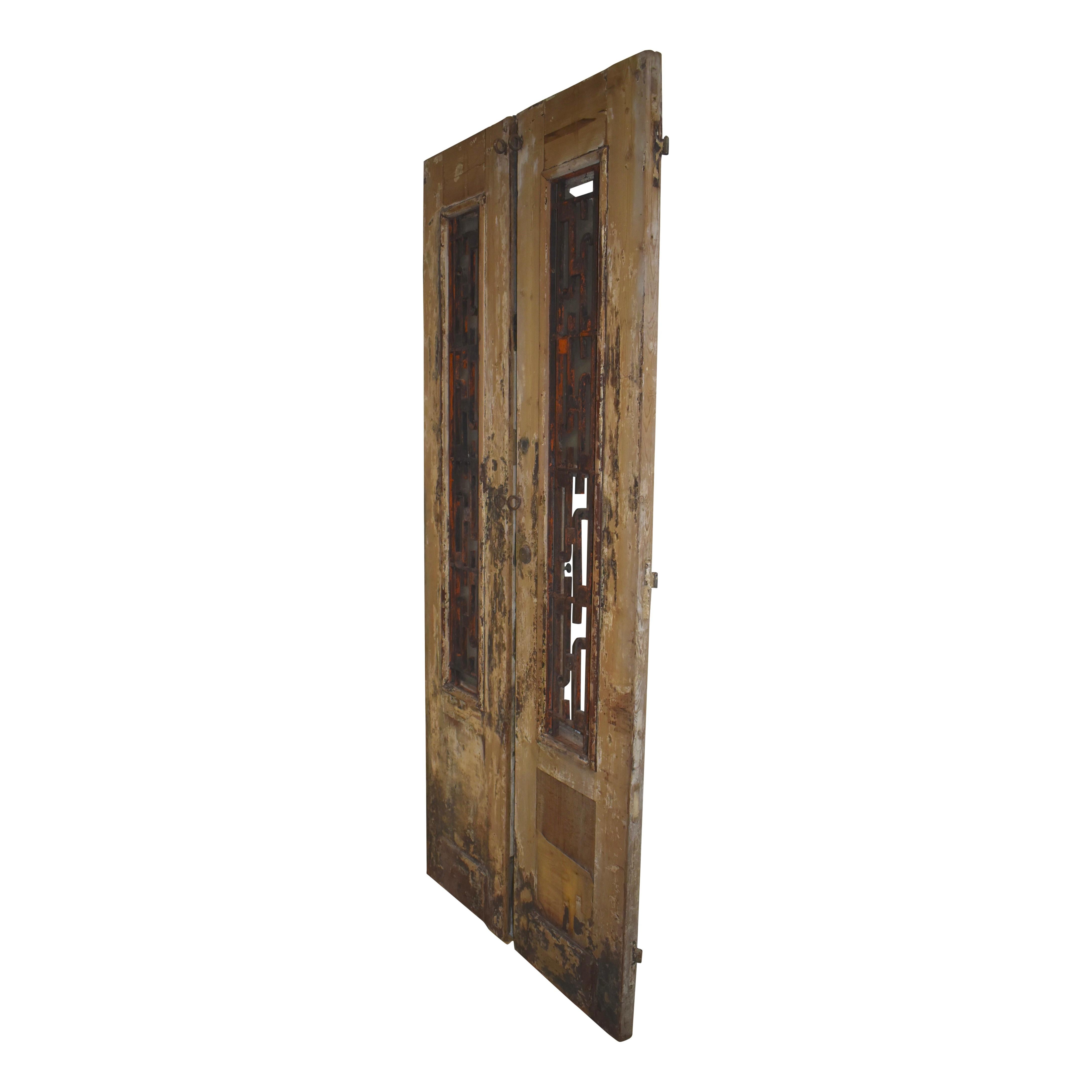 Made of Eastern European pine as is often the case in Egyptian doors, this rustic set features an English Union lock, veneer lower panels, and window frames on the upper halves, enclosing decorative iron work. Each door has frosted vintage glass in