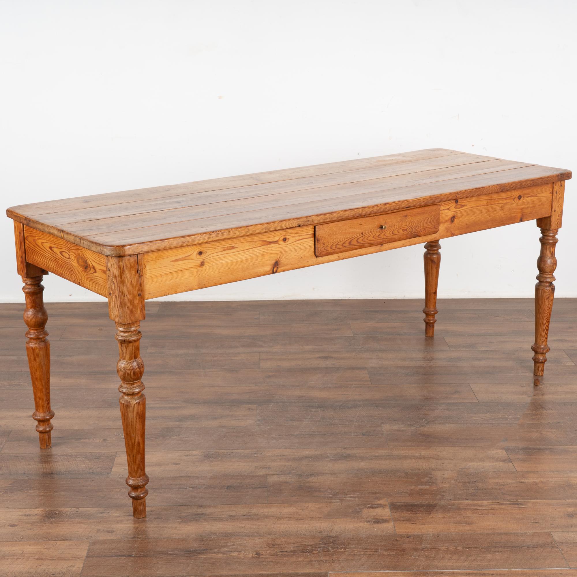 The beauty of this pine farm table comes from the warm aged pine and the lovely turned legs.
It may have originally served as a kitchen work table in a country manor house; note the scratches, dings, stains and age related separation of planks in