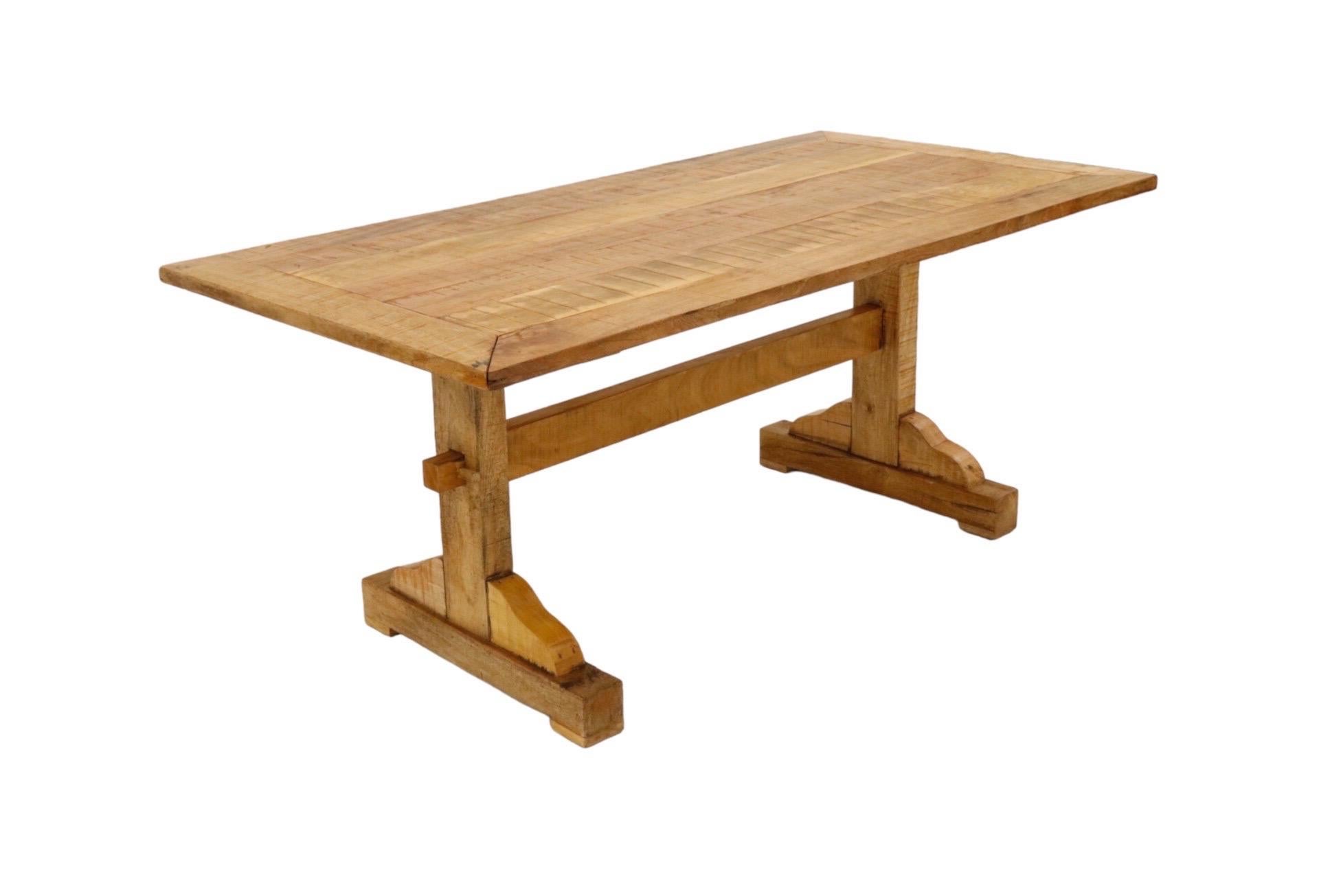 A farmhouse style trestle dining table made of pine. Plank wood forms the tabletop, framed with a wide border. The trestle base consists of two legs supported with a stretcher beam, locked in place with pegs at each side.
