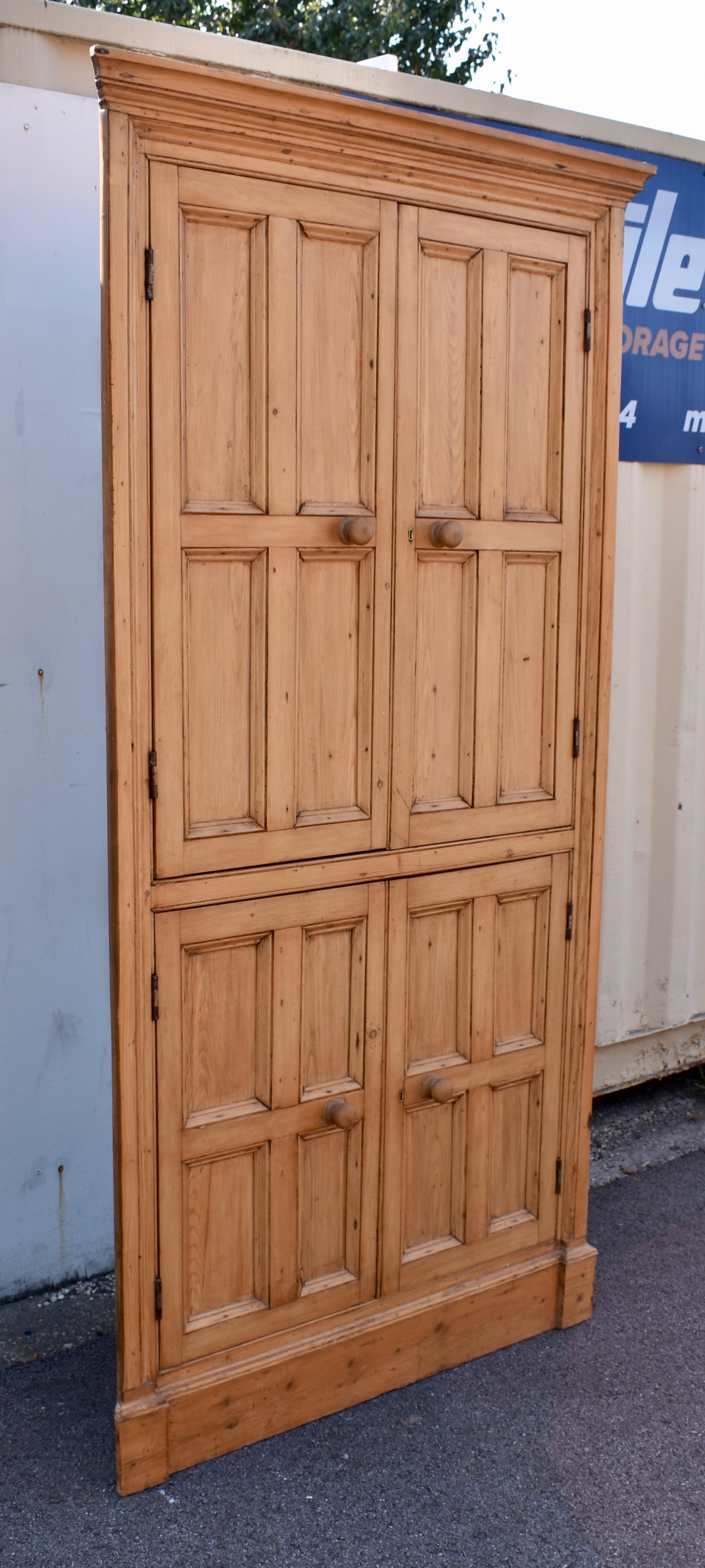 Cada una de las cuatro puertas batientes de este impresionante armario esquinero de pino inglés está dividida en cuatro paneles.  Esto, así como la sencillez de su diseño, en el que la parte frontal de la pieza está en un solo plano, sin esquinas