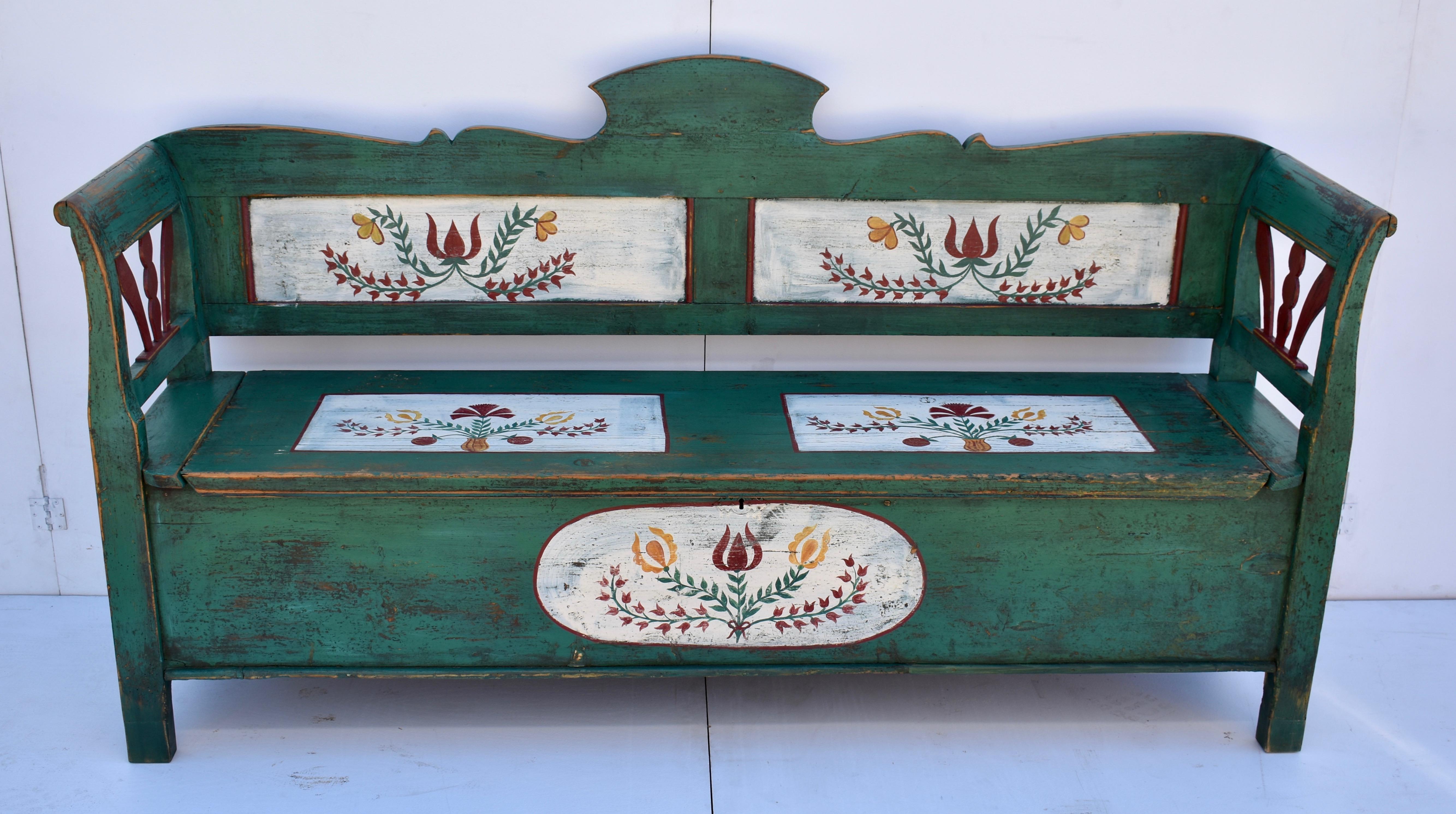 This handsome Hungarian Box Bench has a gently scalloped back rail with a tall cartouche in the center, above two flat panels, recently re-painted in white as a ground for the folk art floral work within. The faux panels on the seat and the oval