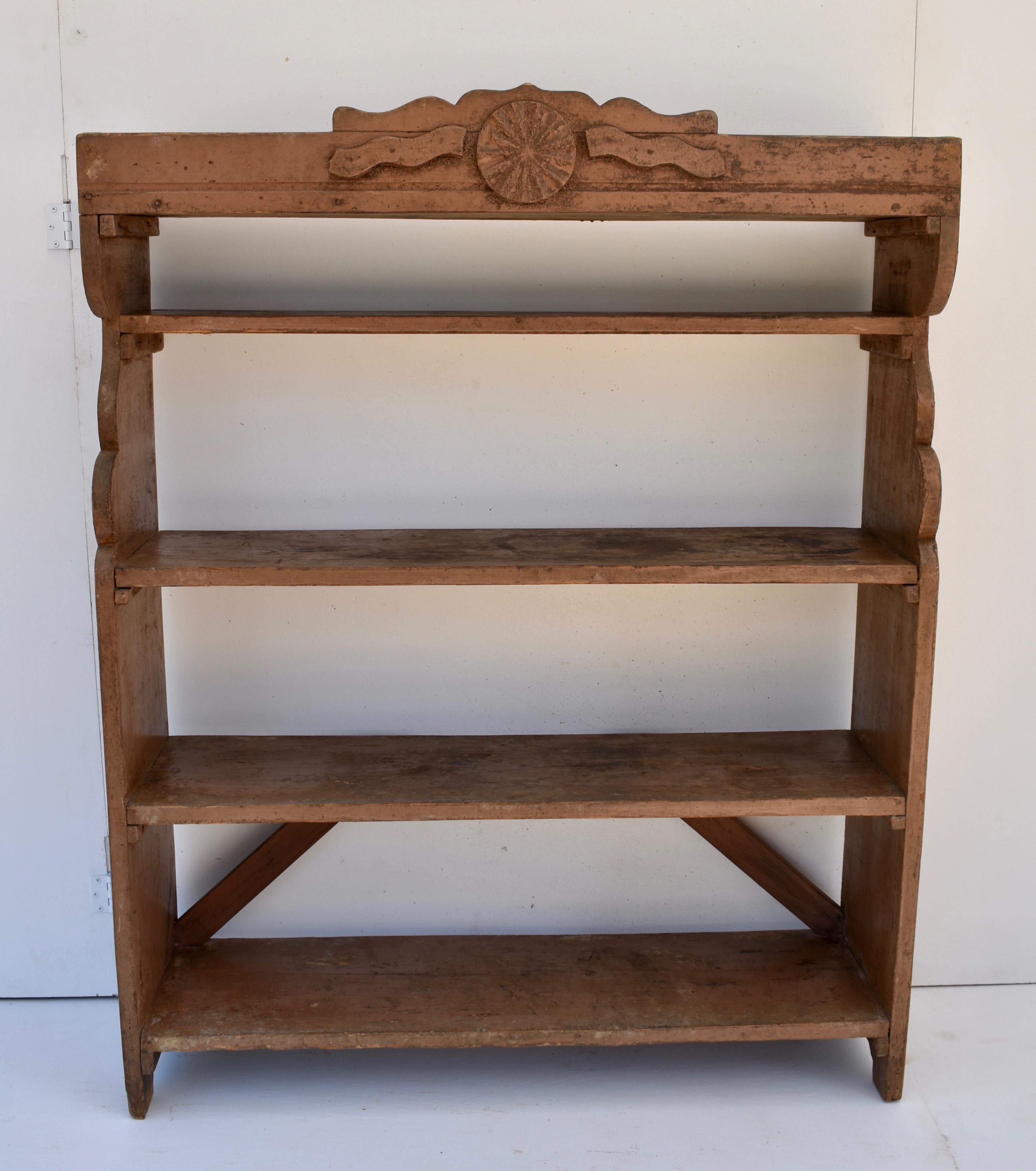 A gallery bearing a central medallion and applied moldings encloses the top shelf. The curvilinear sides support a further four shelves, generously spaced. The lower back is cross-braced for stability. In rich dark rugger brown wax.