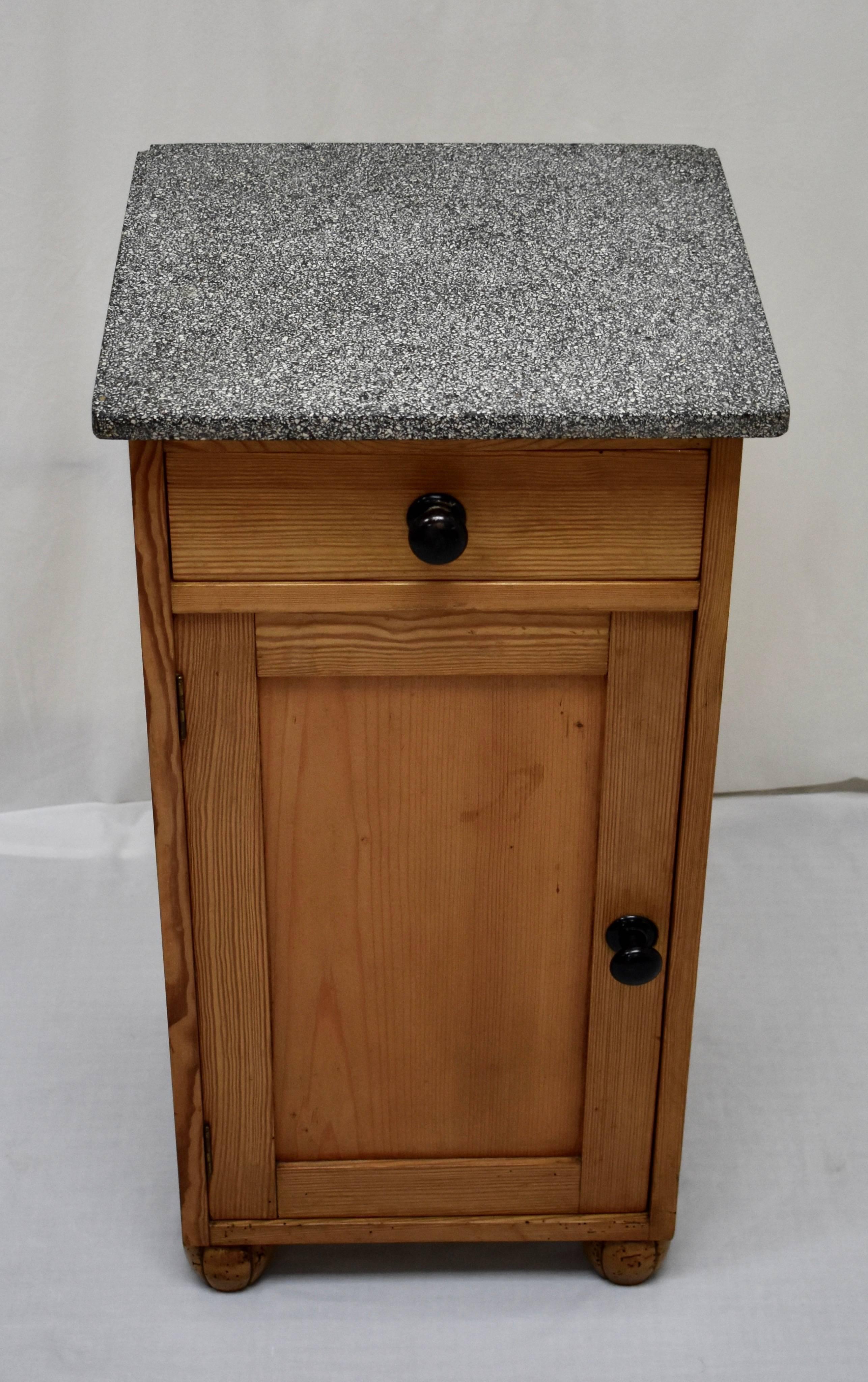 This is a sturdy pine nightstand, in the usual one door, one drawer configuration, with a mottled black and white marble top. The case, with a single dovetailed drawer above a flat paneled door, is without decoration, save for the black metal pulls.