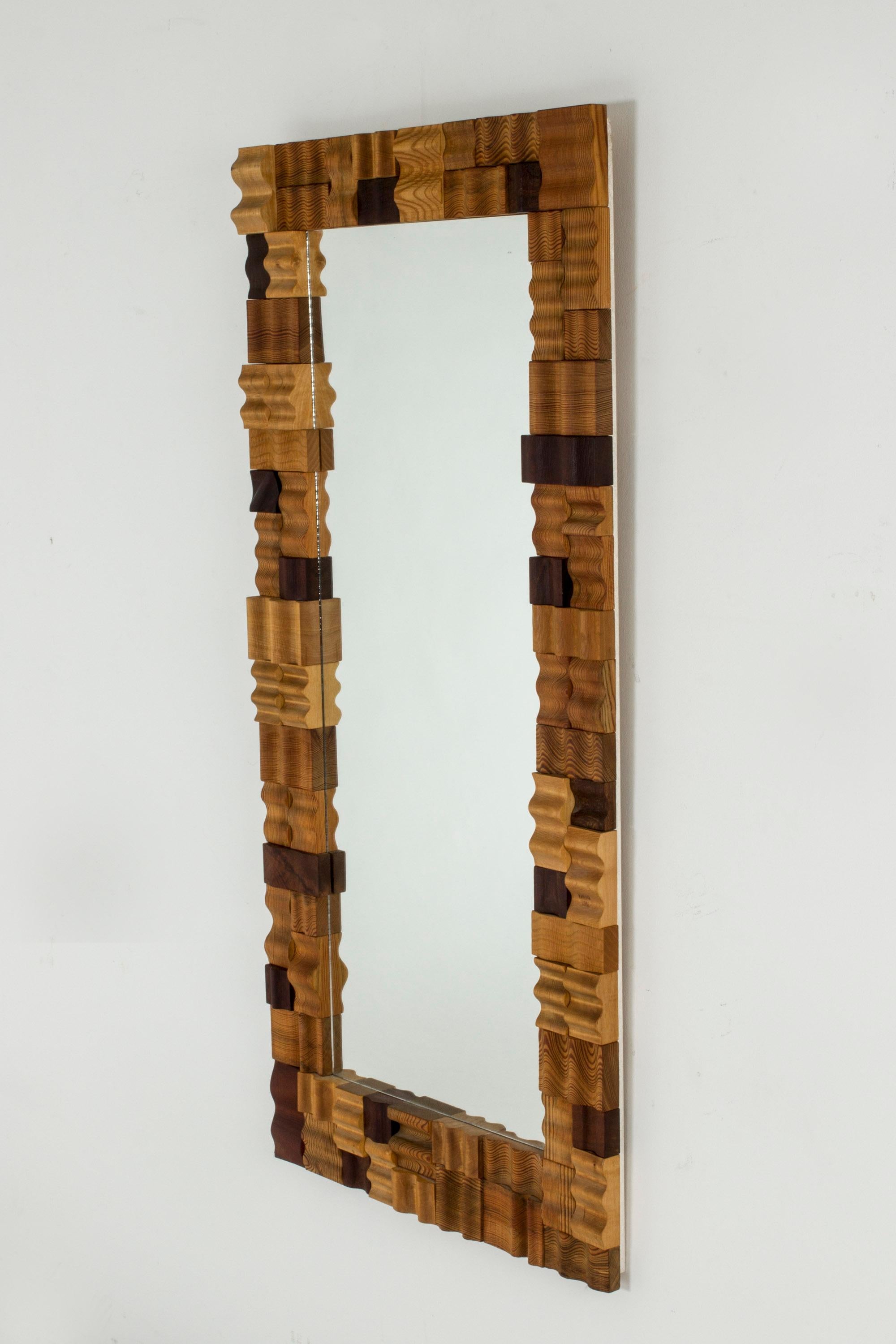 Striking mirror by Gunnar Kanevad, with a frame made from intricately combined pine pieces, all profiled in undulating forms. The distinct wood grain in some pieces, light wood and darker stained appearance of others create a multi-facetted pattern.