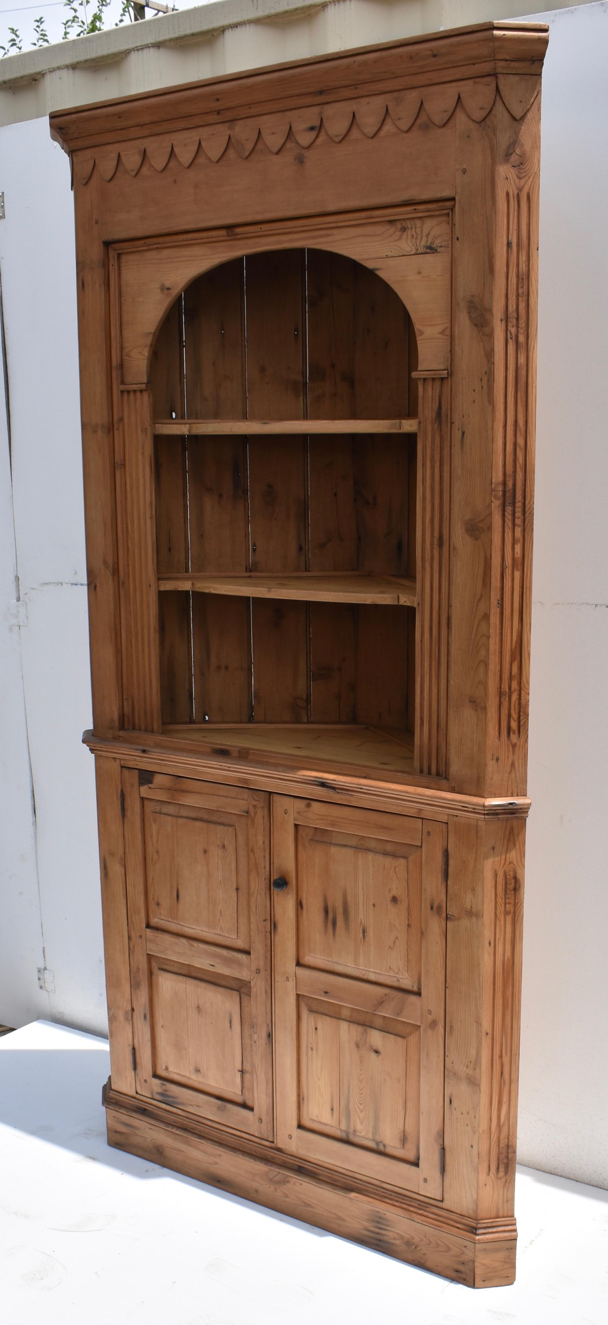 This is a very attractive pine corner cupboard, tall and shallow and full of character.  In the upper section a deep frieze is crowned with bold molding and applied gadroons, incised fluting on the chamfered front corners framing an arched fascia,