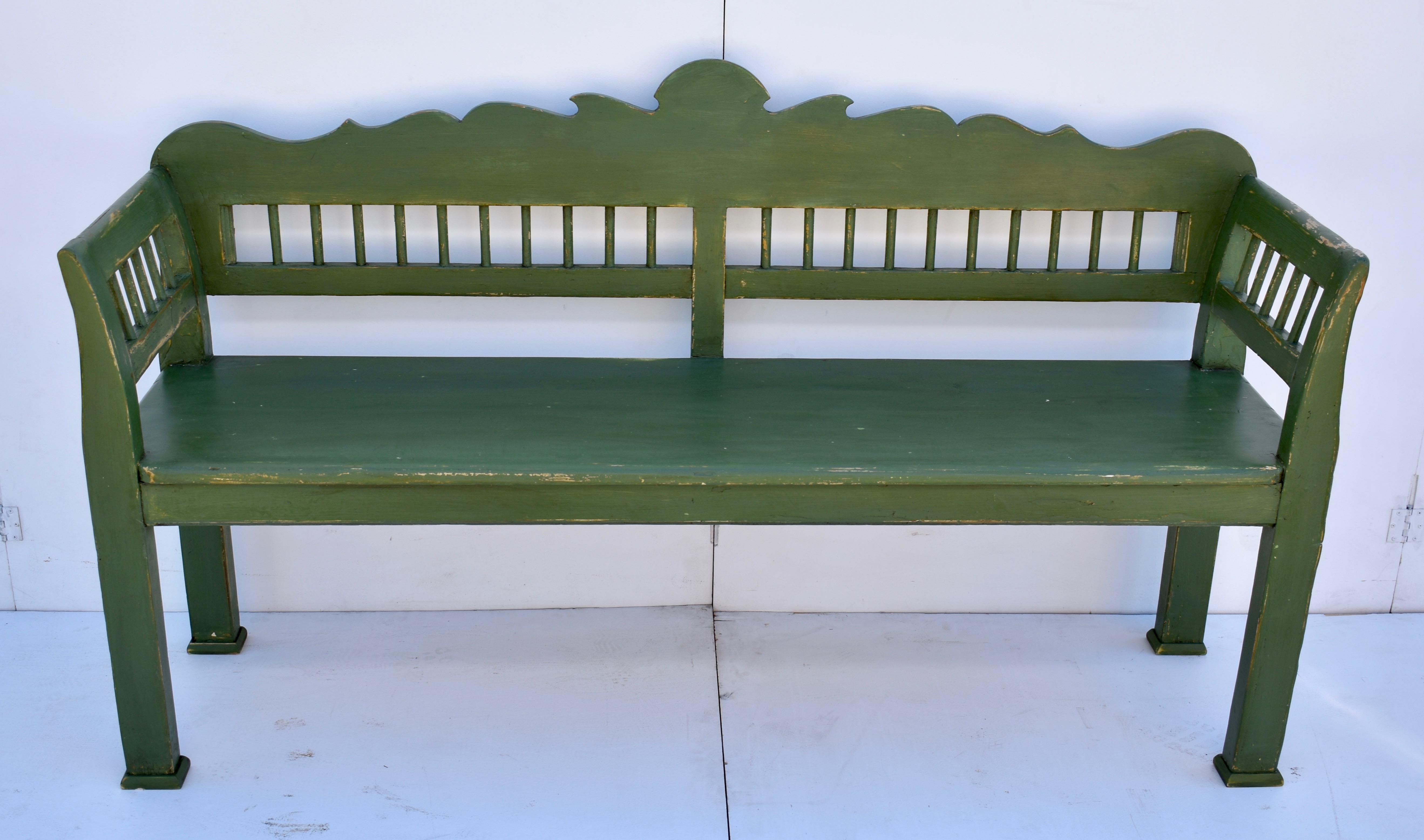 This versatile pine bench has a boldly scalloped top rail, with a row of plain dowels beneath. The arms are slightly scrolled and the integral legs are straight from the seat level to the floor. In old worn green paint.


