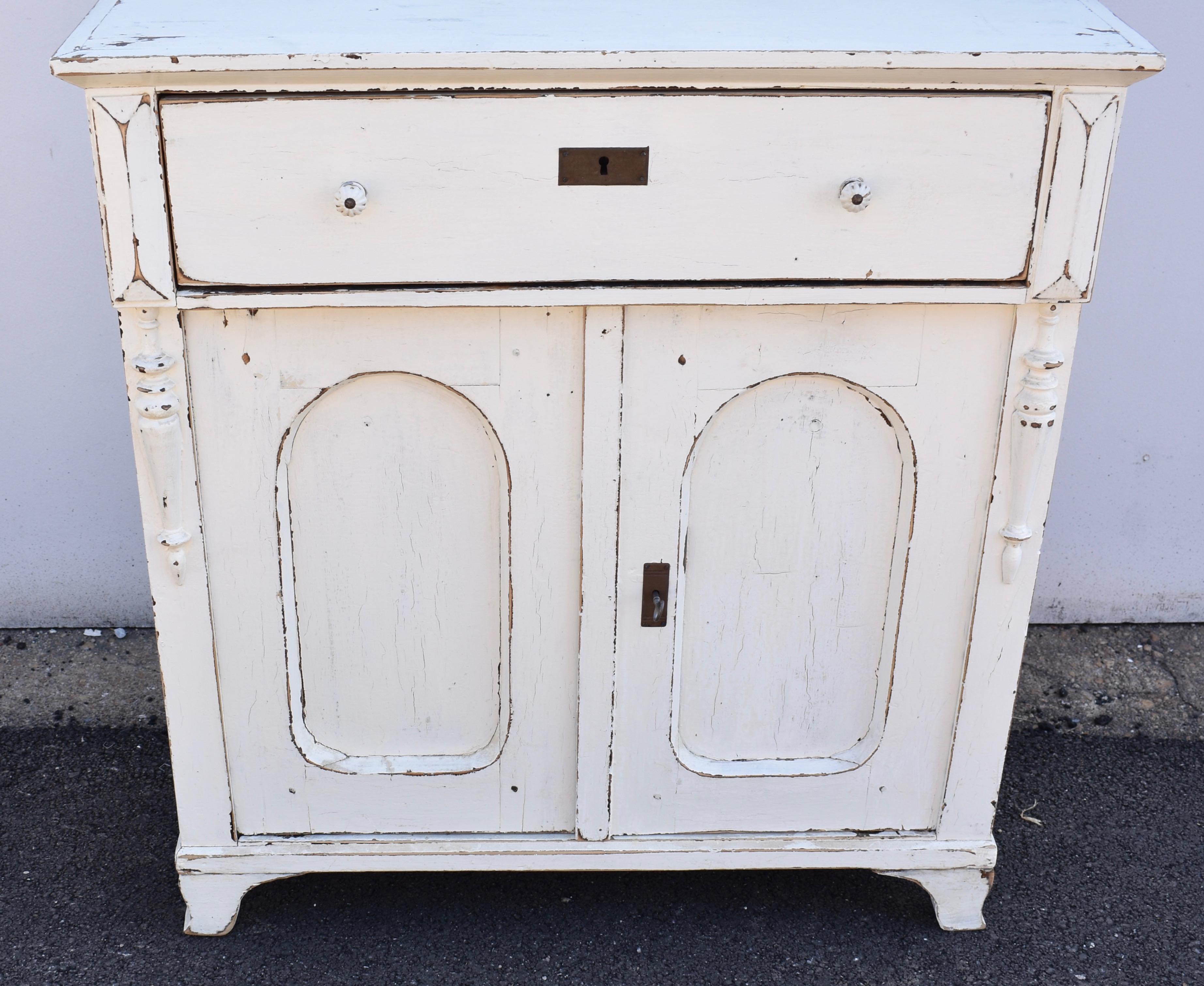 This unusually shallow painted dresser base has such a lovely form.  The top is flat with a plain crown molding.  There is a single deep hand-cut dovetailed drawer above two doors with arched top flat panels.  The front corners have a long pyramid