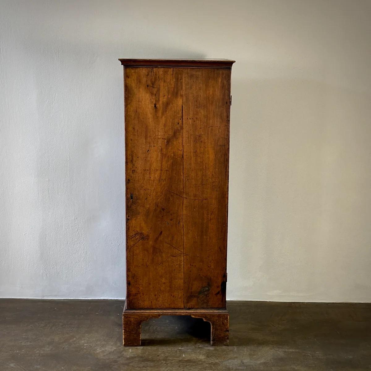 18th-century pine pedestal cupboard from England, standing on original bracket feet. This plain yet elegantly constructed piece features a plinth base and internal shelving, providing a unique combination of historical charm and practical