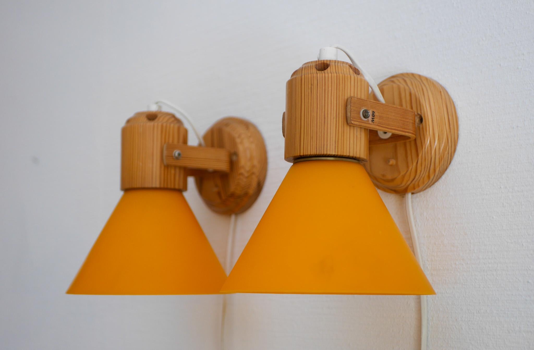 A pair of modern Scandinavian vintage pine sconces/ wall lighing, which have a orange acrylic cone. The lamps are from to Solbackens svarveri, Sweden. The lamps has a classic shape for the 1970s, the orange lampshades gives a very nice light, but is