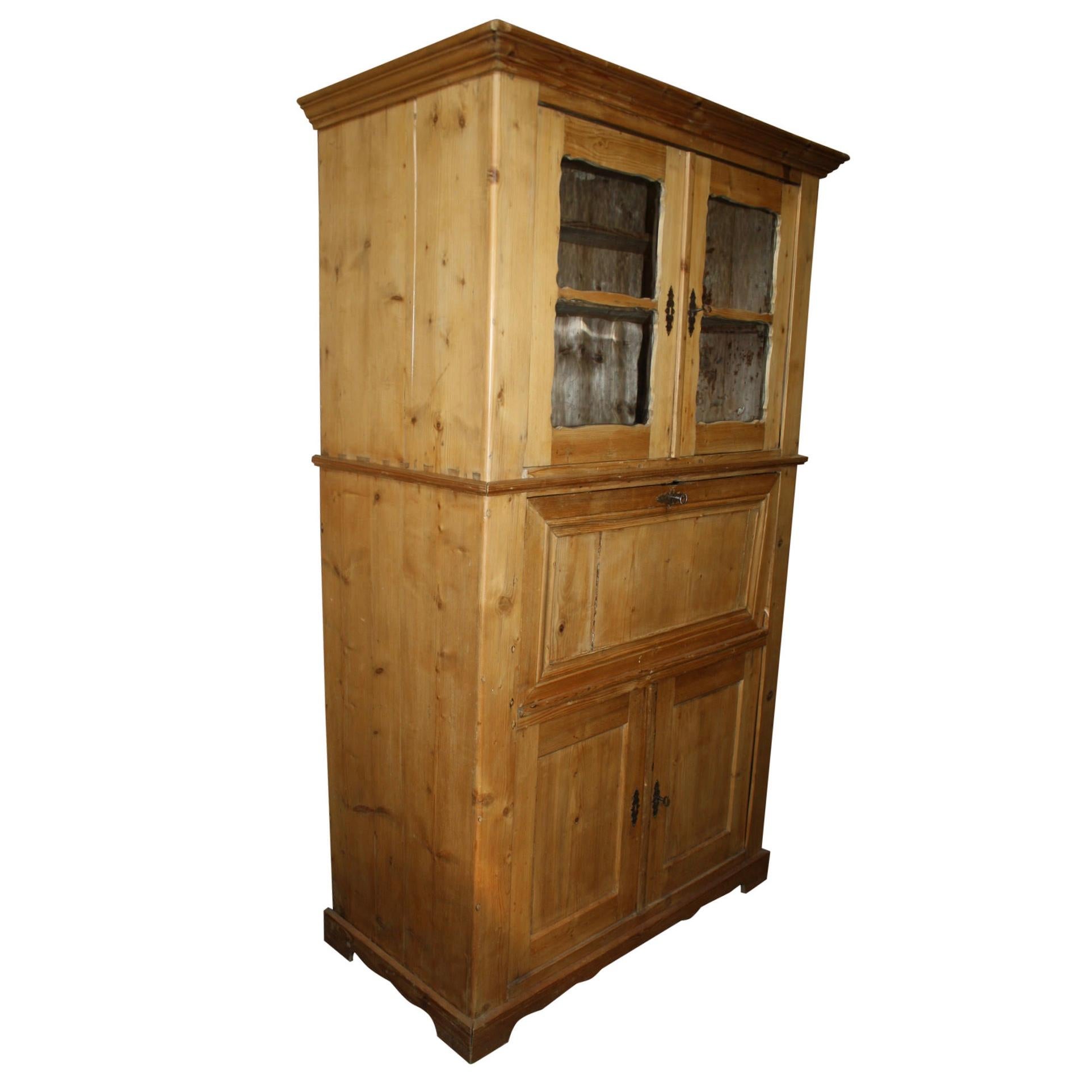 Comprised of three sections, this tall, pine secretary has generous storage and practical organization. It features an upper cabinet with two glass doors and single shelf, a drop-down front that opens to five small drawers, and a lower cabinet with