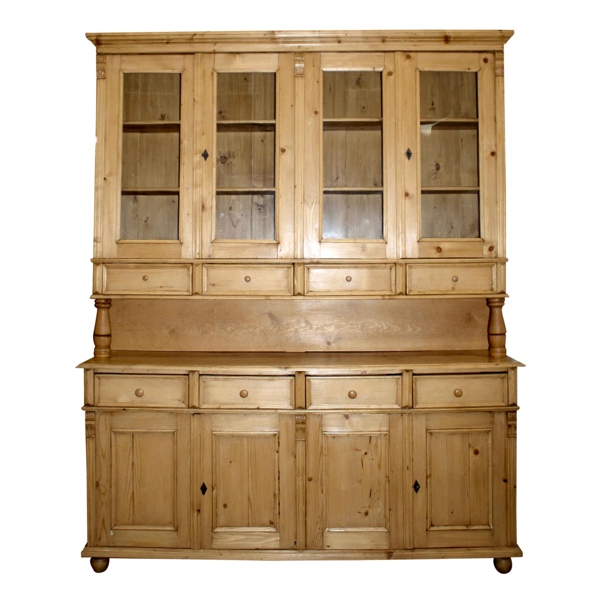 Generous in size and storage, this pine sideboard is comprised of a top with two sets of double glass doors above four drawers and a base with two sets of double recessed panel doors below four additional drawers. The drawers have dovetail corners