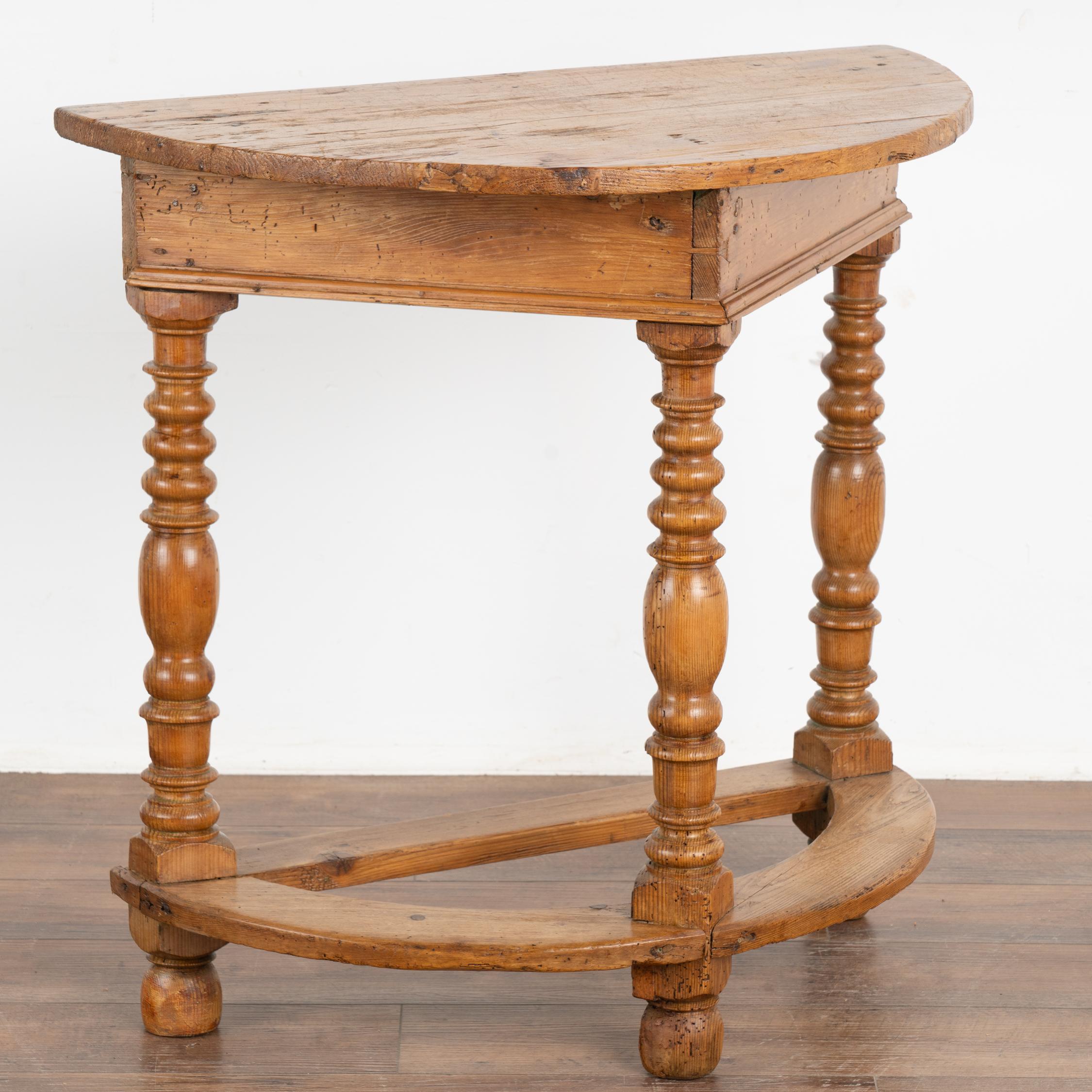 It is the generations of use that create the deep, attractive aged patina of this pine side table.
The three decorative turned legs with trestle base create visual appeal to the half-moon shape of the table.
Professionally restored, this table is