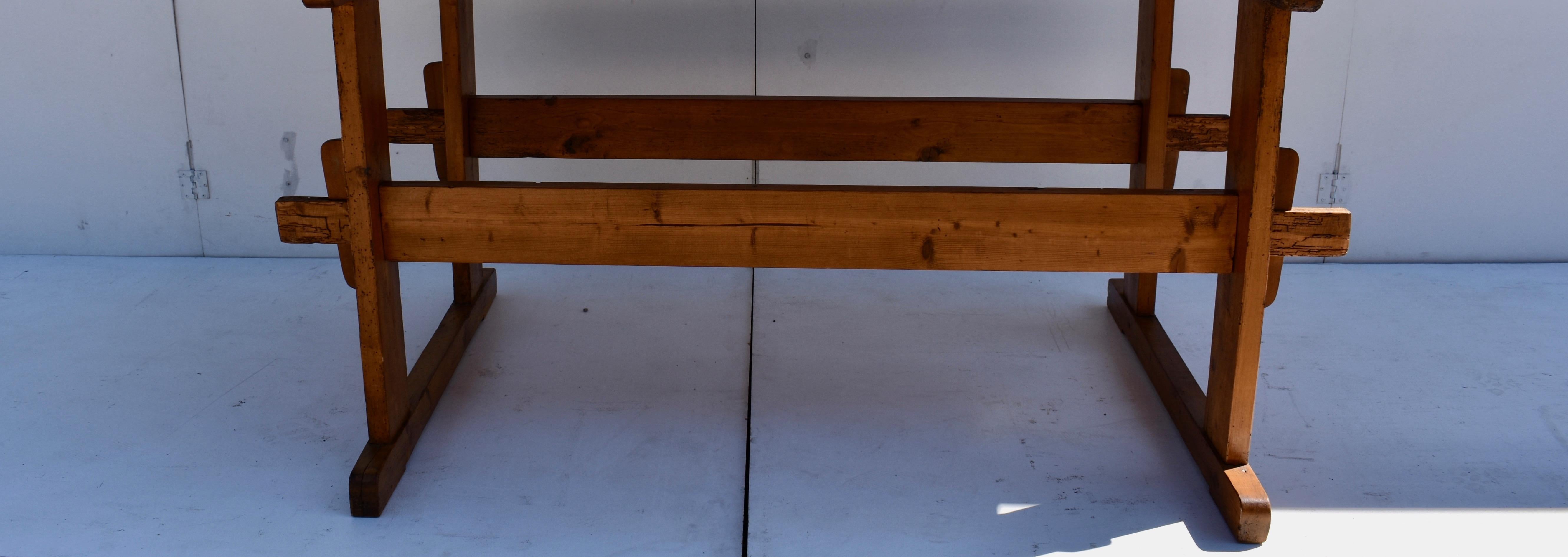 This handsome work table has a beautiful top over one inch thick, nicely chopped and sliced along both sides. The trestle ends have two uprights, a long top member with overhang and a long sled-type foot. The ends are joined with double stretchers
