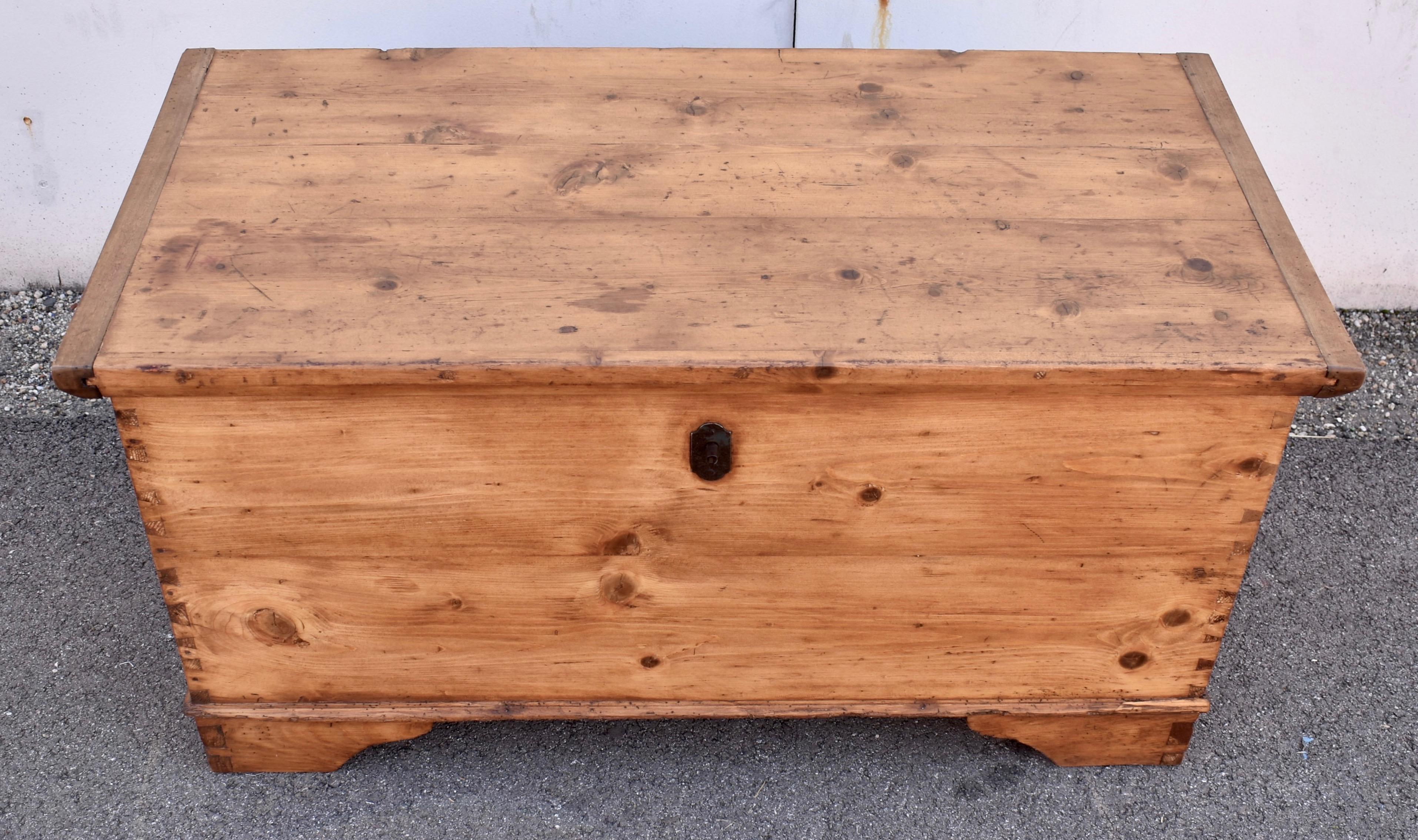 Diese schlichte und einfache Deckentruhe aus Kiefernholz besteht aus einer handgeschnittenen Konstruktion mit Schwalbenschwanz und Zapfen.  Der Deckel ist an beiden Enden mit Hartholzbrettern versehen und lässt sich an langen Eisenscharnieren