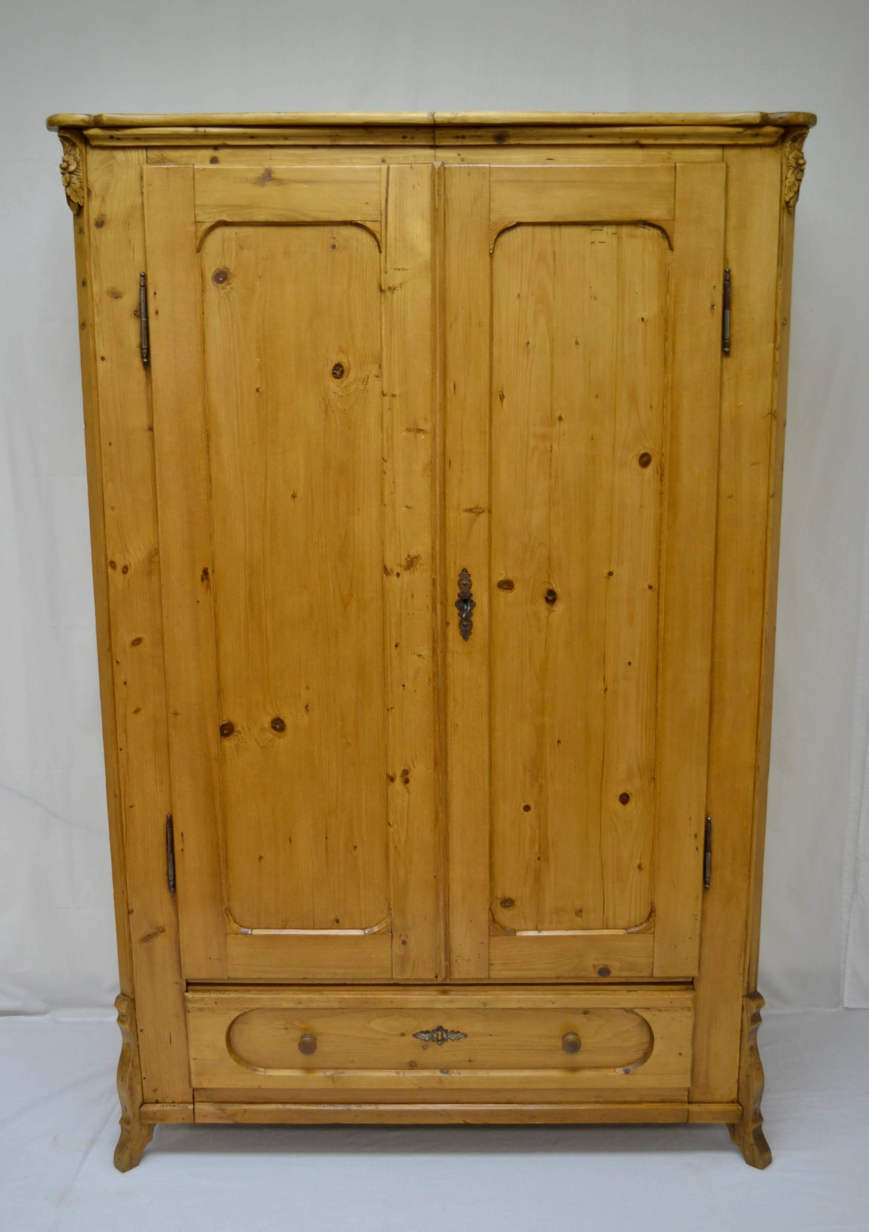 This lovely two door pine armoire features a scalloped crown with rounded corners and hand-carved oak leaf and acorn corbels mounted to the chamfered front corners. The panelled doors are mounted on iron fiche hinges allowing them to open a full 180