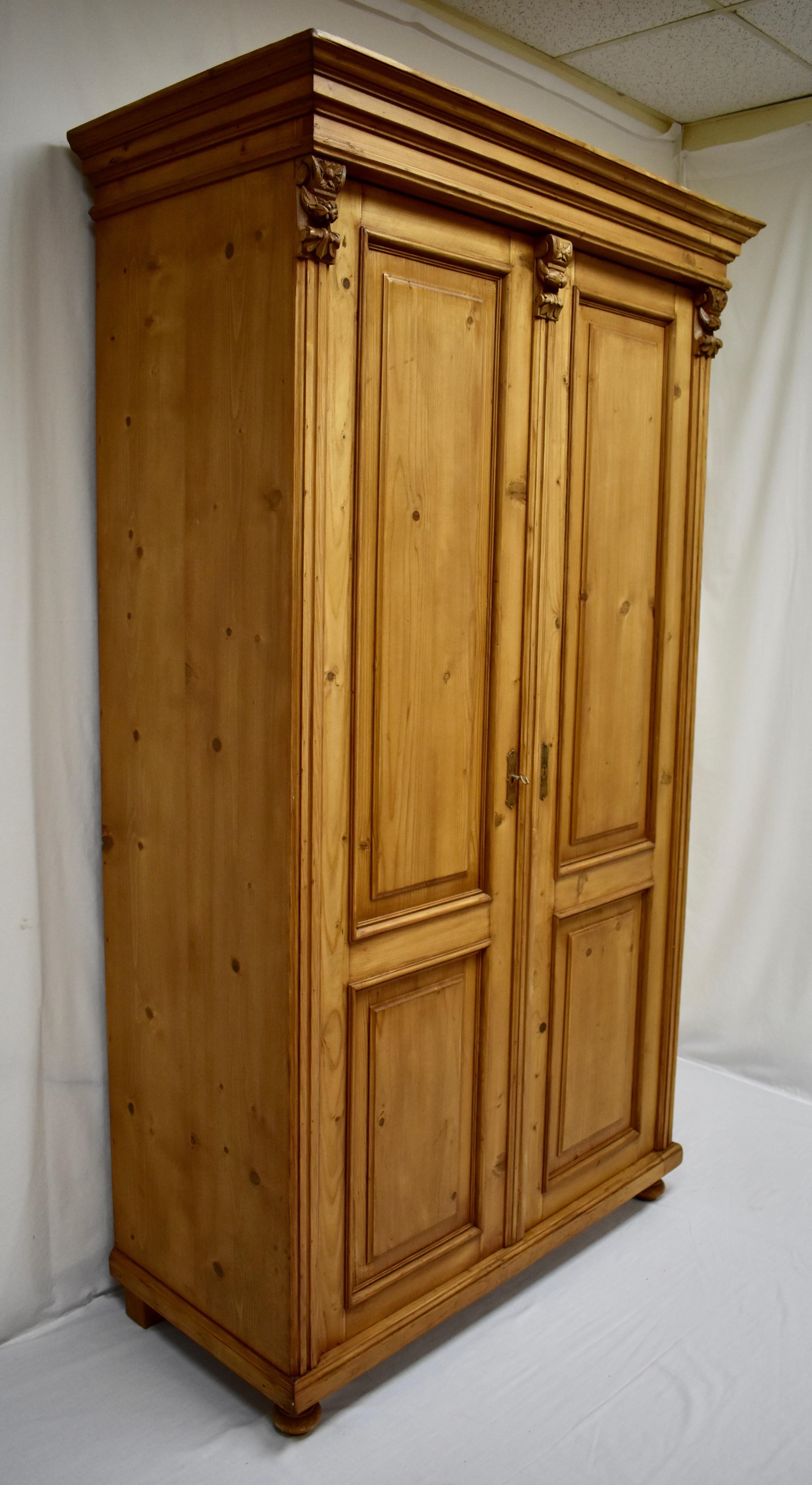 This is a very attractive tall and handsome pine armoire. Beneath a bold crown molding are two doors, each with two raised panels. These are flanked and separated by convex fluted molding mounted by very elaborate fruitwood corbels. At some point a
