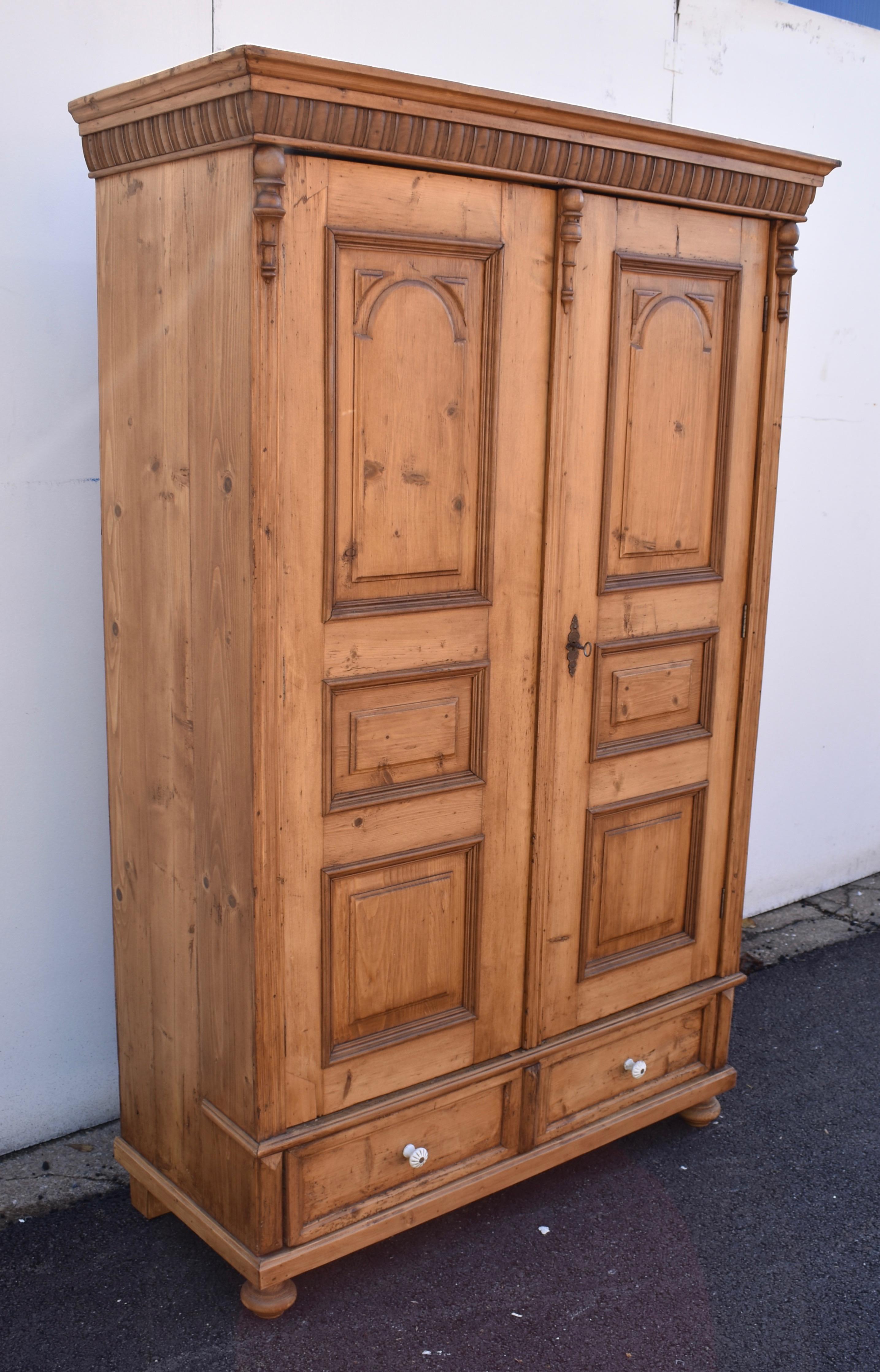 This is a small armoire with a great deal of presence.  The crown is bold with a pine ogee atop a deep tier of hardwood gadrooning.  Beneath are two doors, flanked and separated by fluting capped with hardwood split balusters.  Each door has three