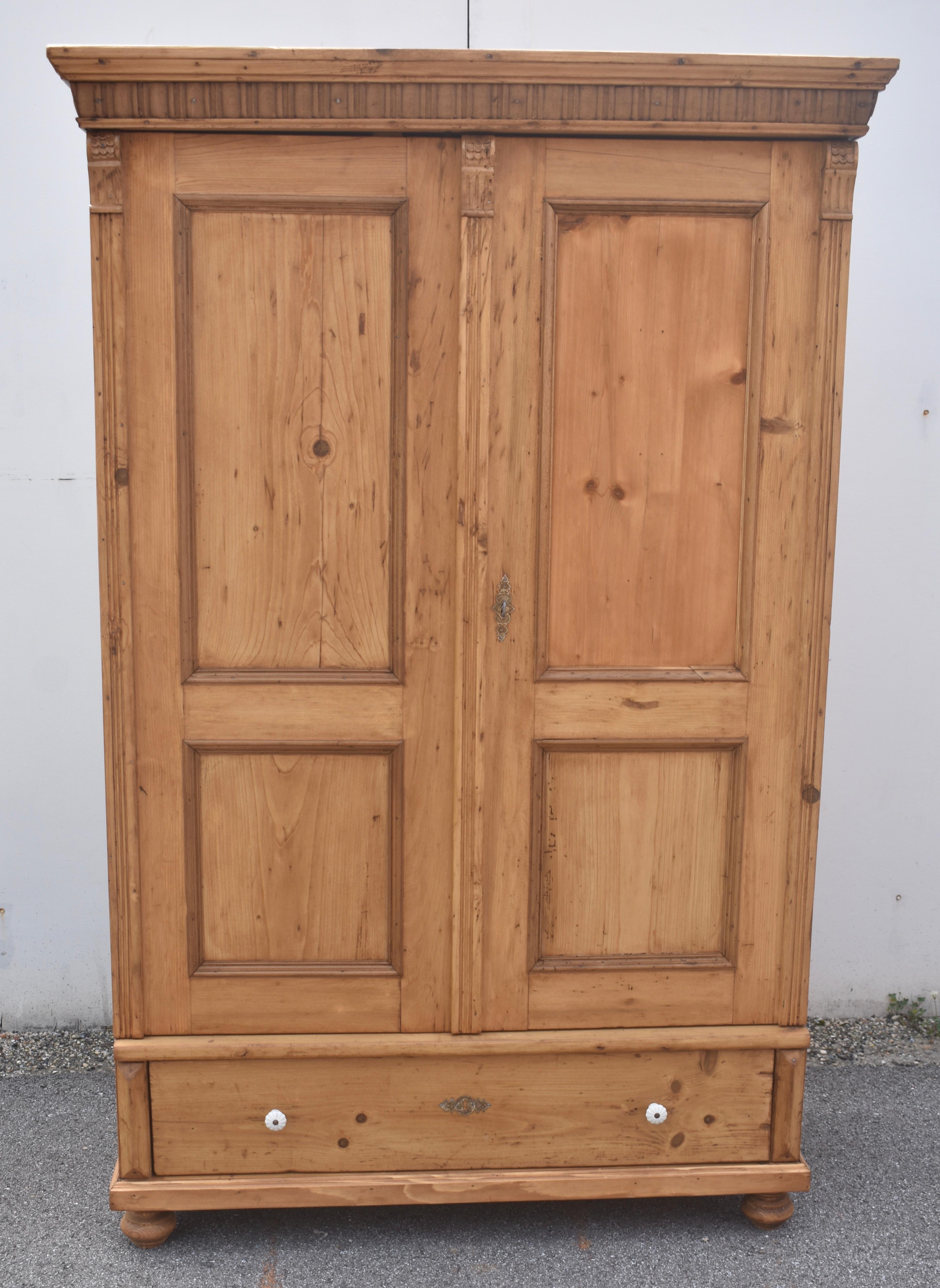 The bold crown of this typical Central European pine armoire comprises a pine ogee molding above a strip of hardwood gadroon molding.  The wide swinging doors each have one long flat panel and one short, secured by hardwood mullions.  Reeded molding
