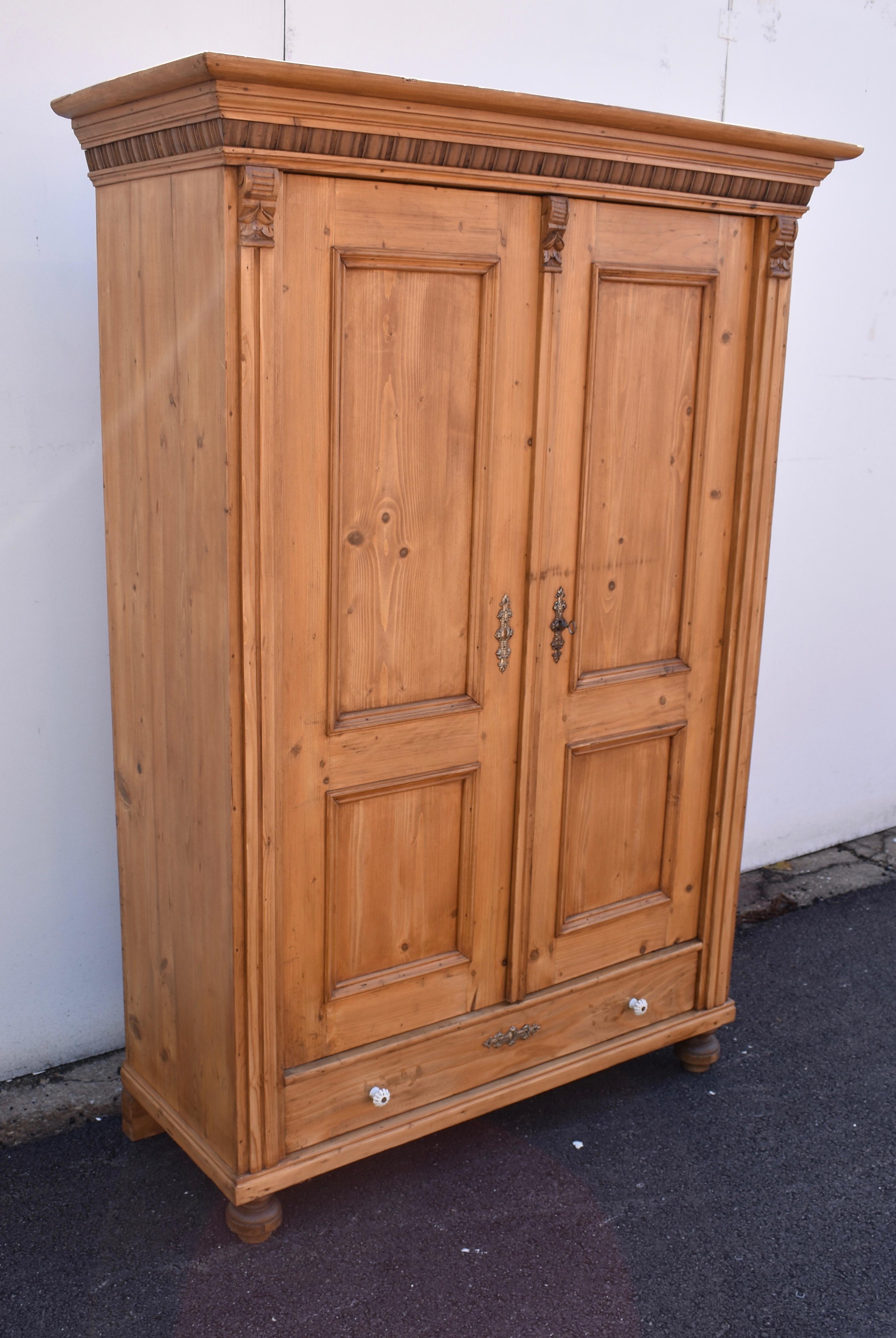 This pretty little armoire has many of the features that make antique Hungarian pine furniture so attractive. The beautiful crown is built of five tiers of molding. Including a row of hardwood gadrooning. The front corners border the doors with