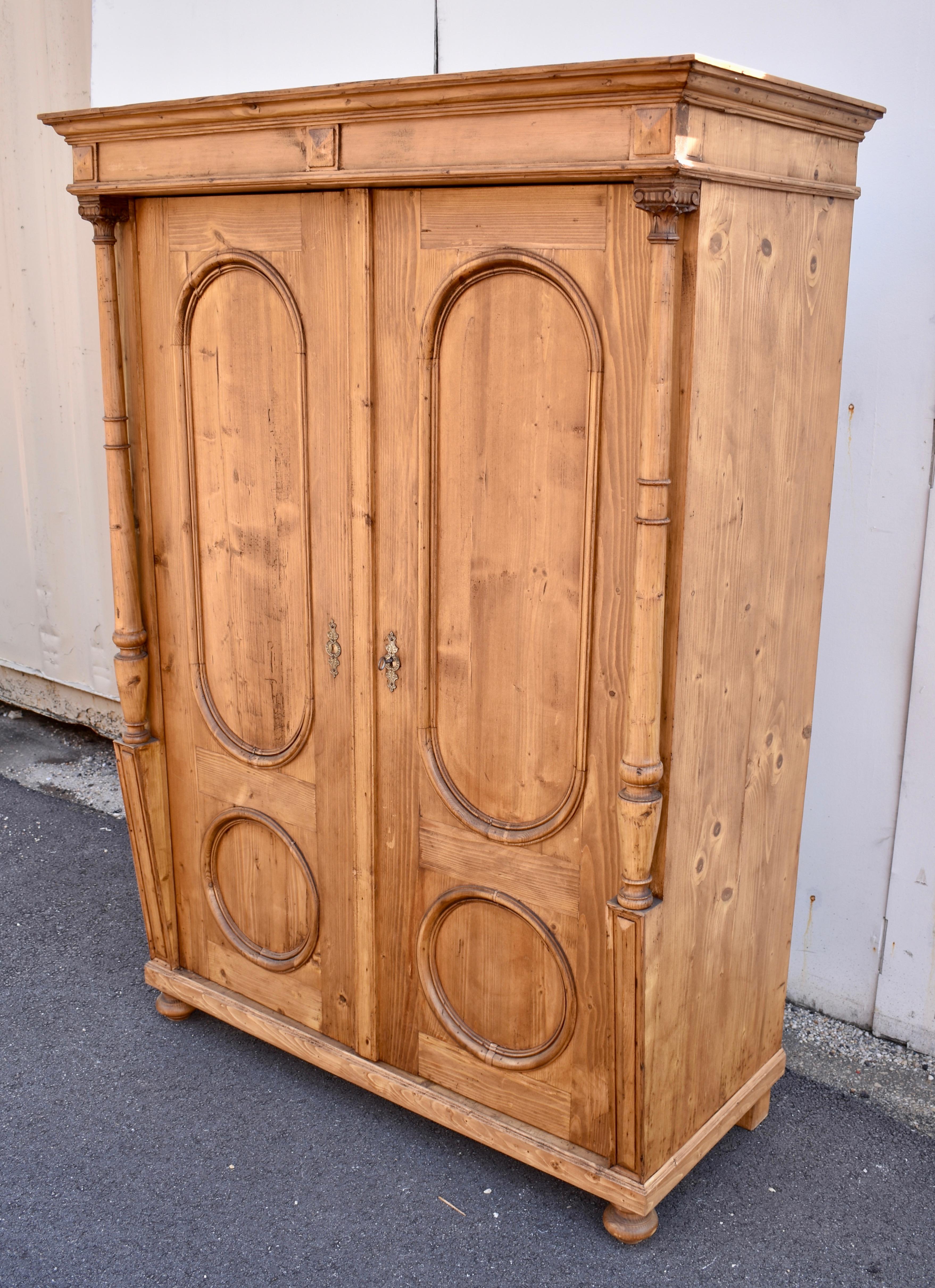 This small armoire has considerable presence.  The bold crown sits above a frieze with three applied pyramids.  This stands proud of the doors as if supported by the full turned columns that adorn the front corners, standing on wedge-shaped bases