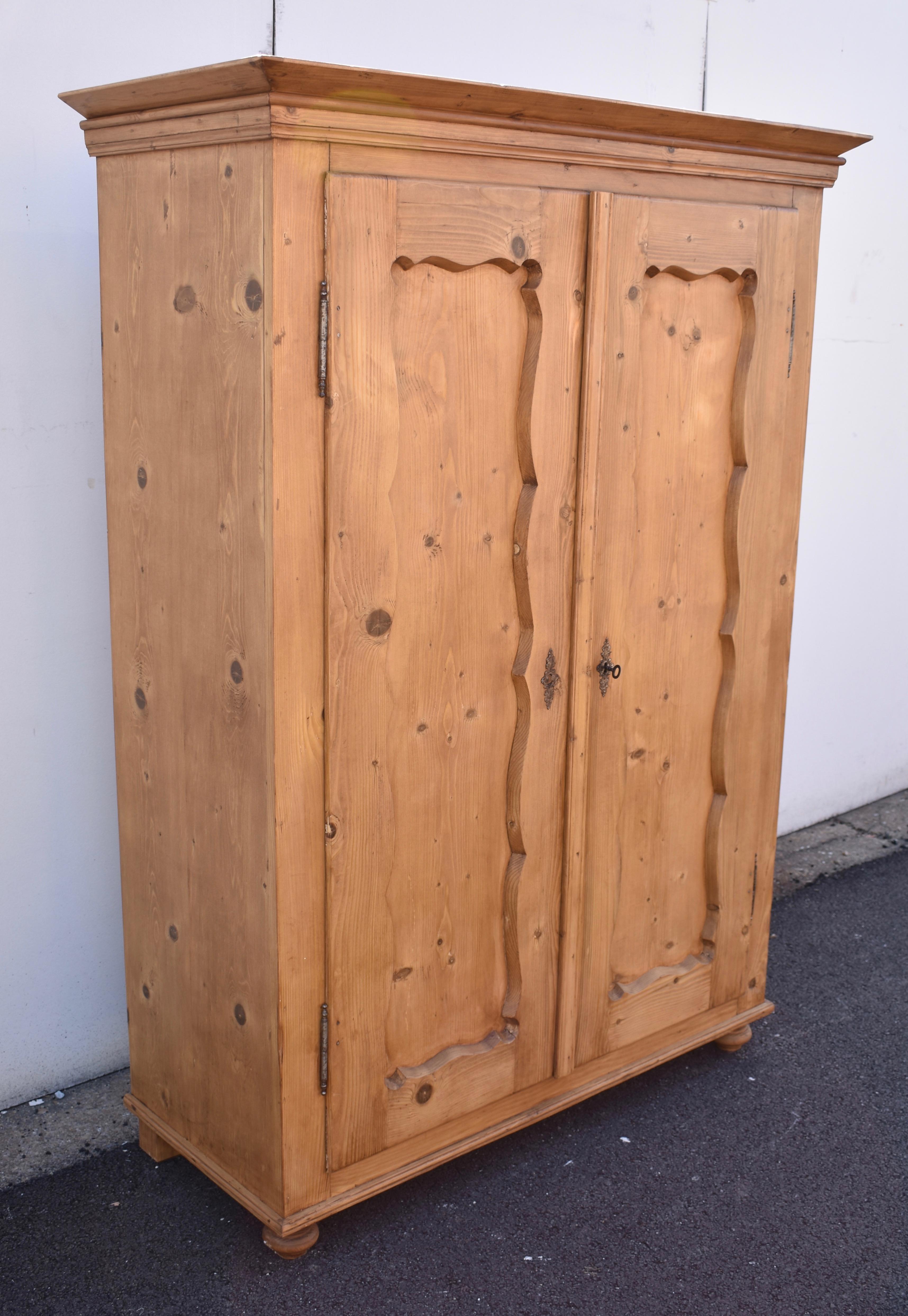 This sturdy little armoire has simple but interesting lines and a beautiful honey color. The crown is plain but elegant with a reeded frieze beneath the flat corona molding. The case is entirely without adornment. The two doors are mounted on