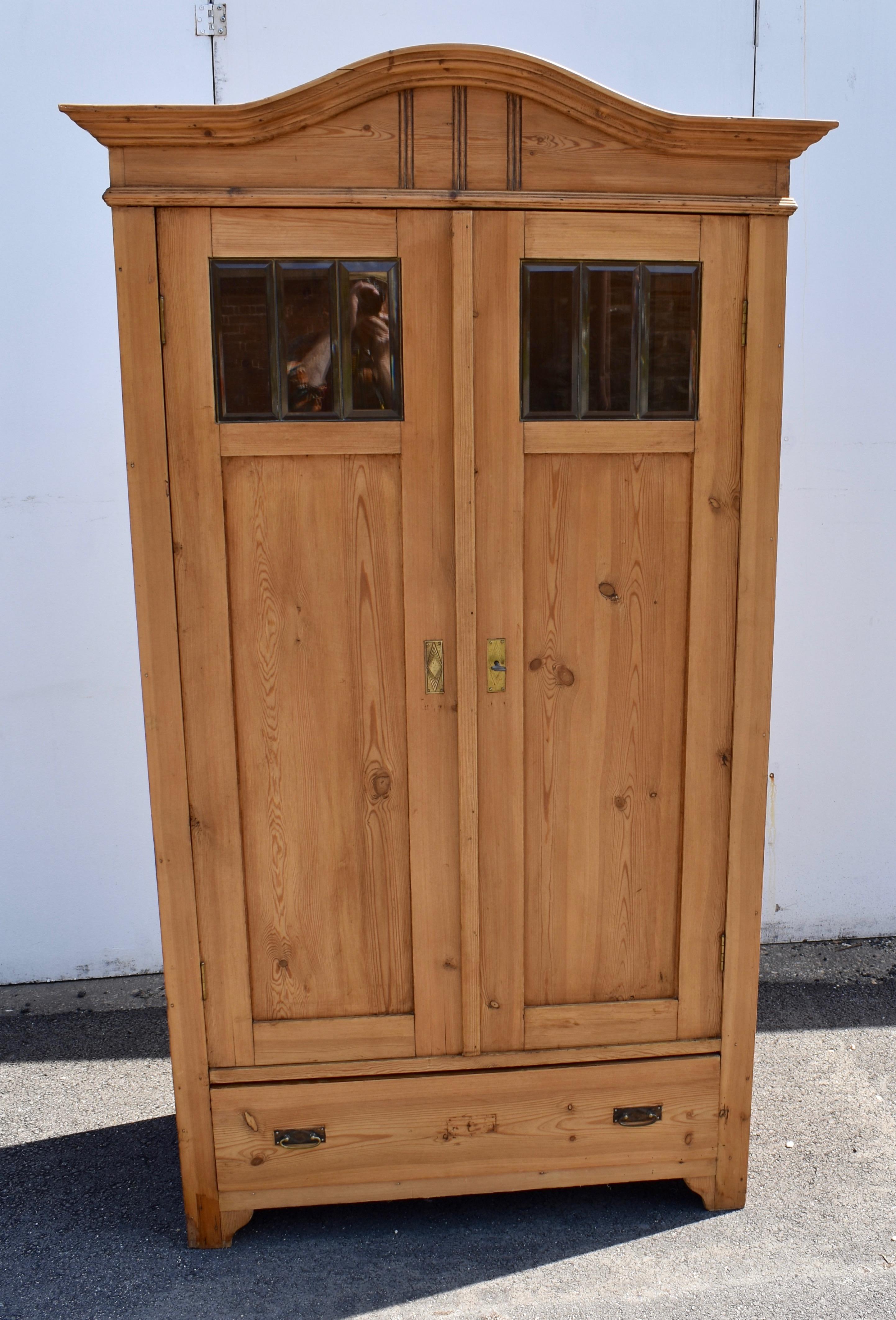 The arched front frieze of this handsome armoire, with its three rows of vertical reeds is original but the bold crown molding has been replaced. Each door has a long flat pine panel beneath a square panel comprising three panes of beveled glass.