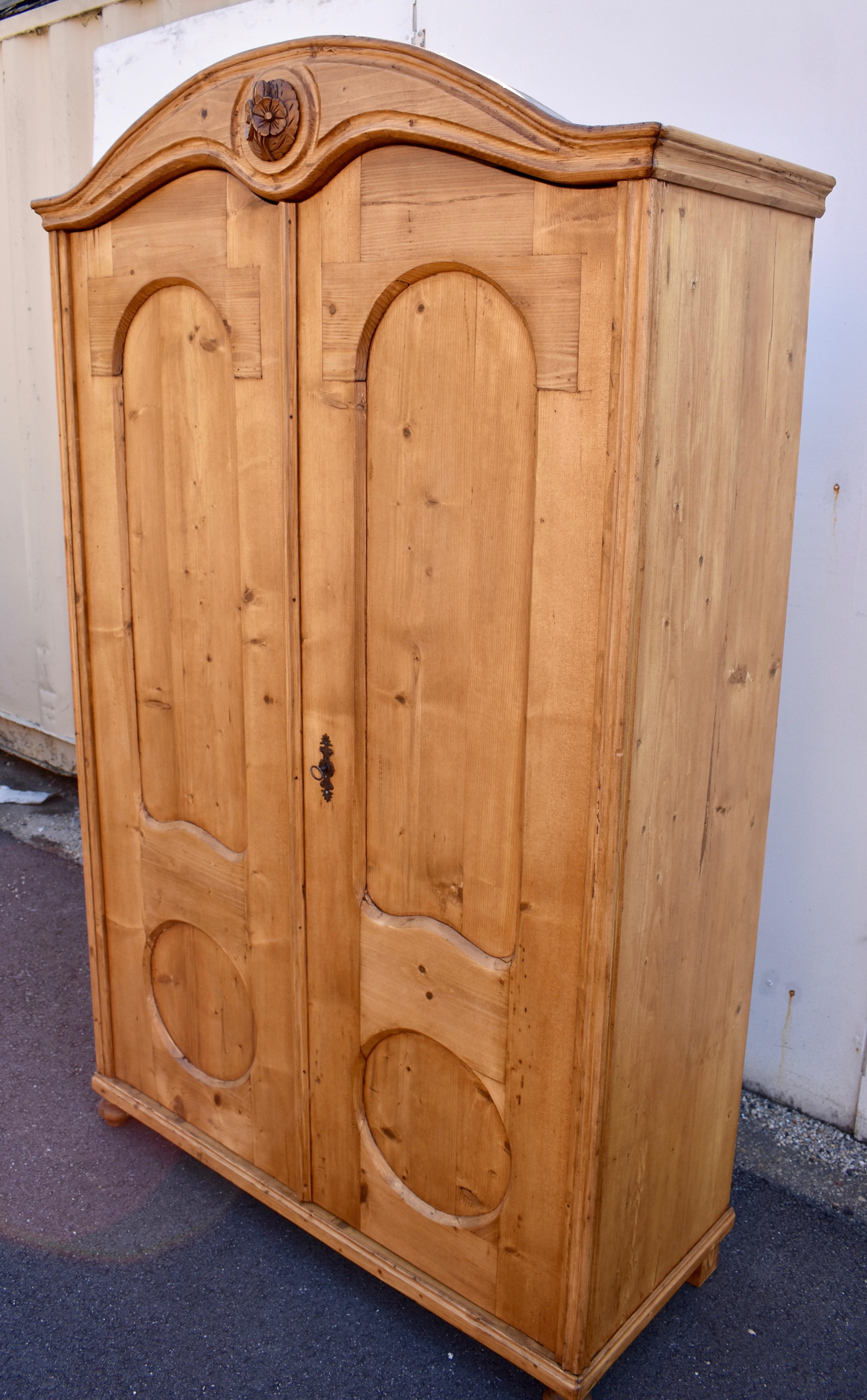 This is an interesting two door armoire with a very attractive form. The bonnet-top crown has a wonderful “swooping” line on top with a Queen Anne style double arch beneath.  In the center of the crown is mounted an applied carved hardwood floral