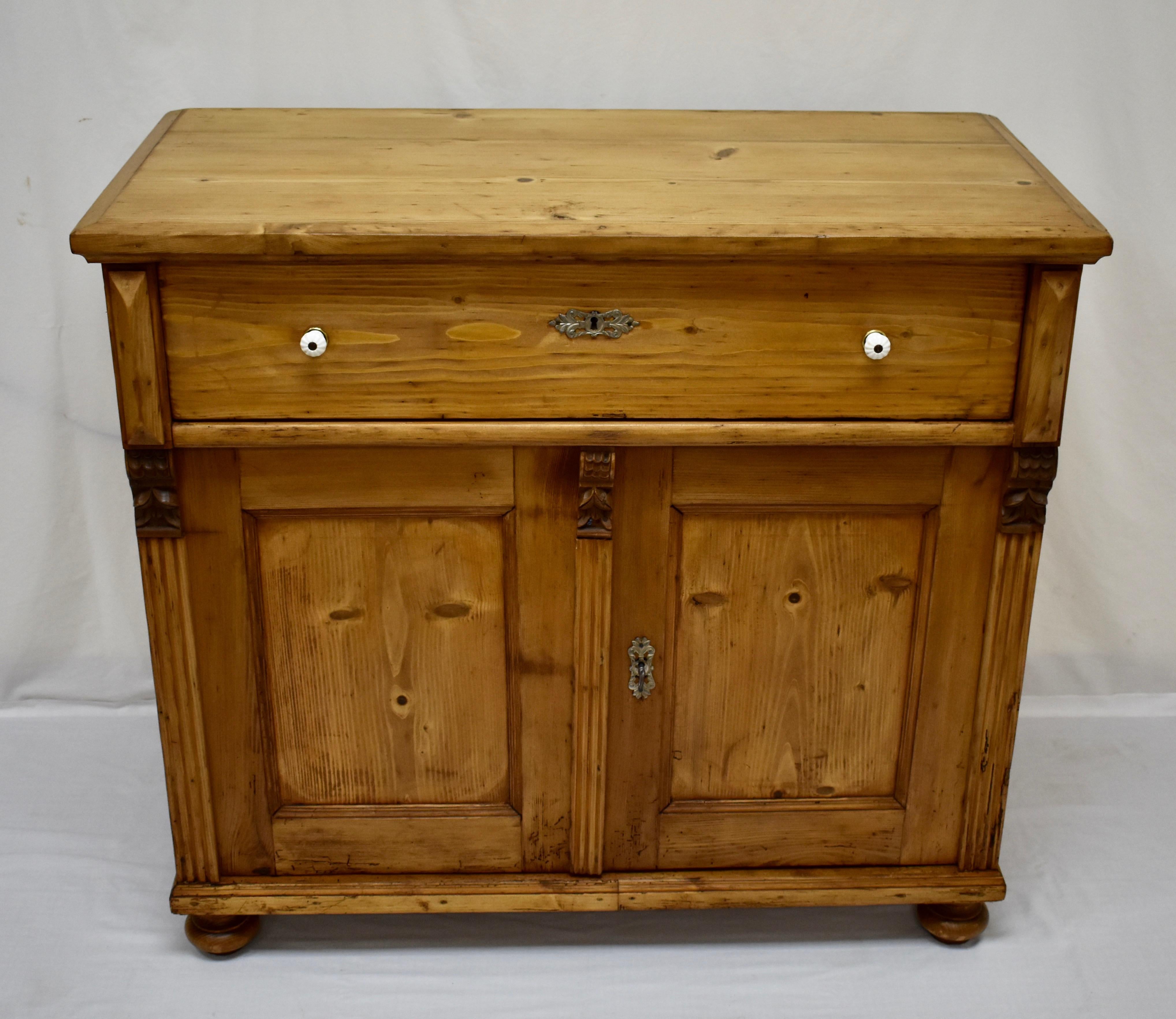 This handsome dresser base has a two board top trimmed with crown molding. A single long hand-cut dovetailed drawer with original ceramic knobs sits above two flat paneled doors, flanked and separated by fluting and oak corbels. The doors open on