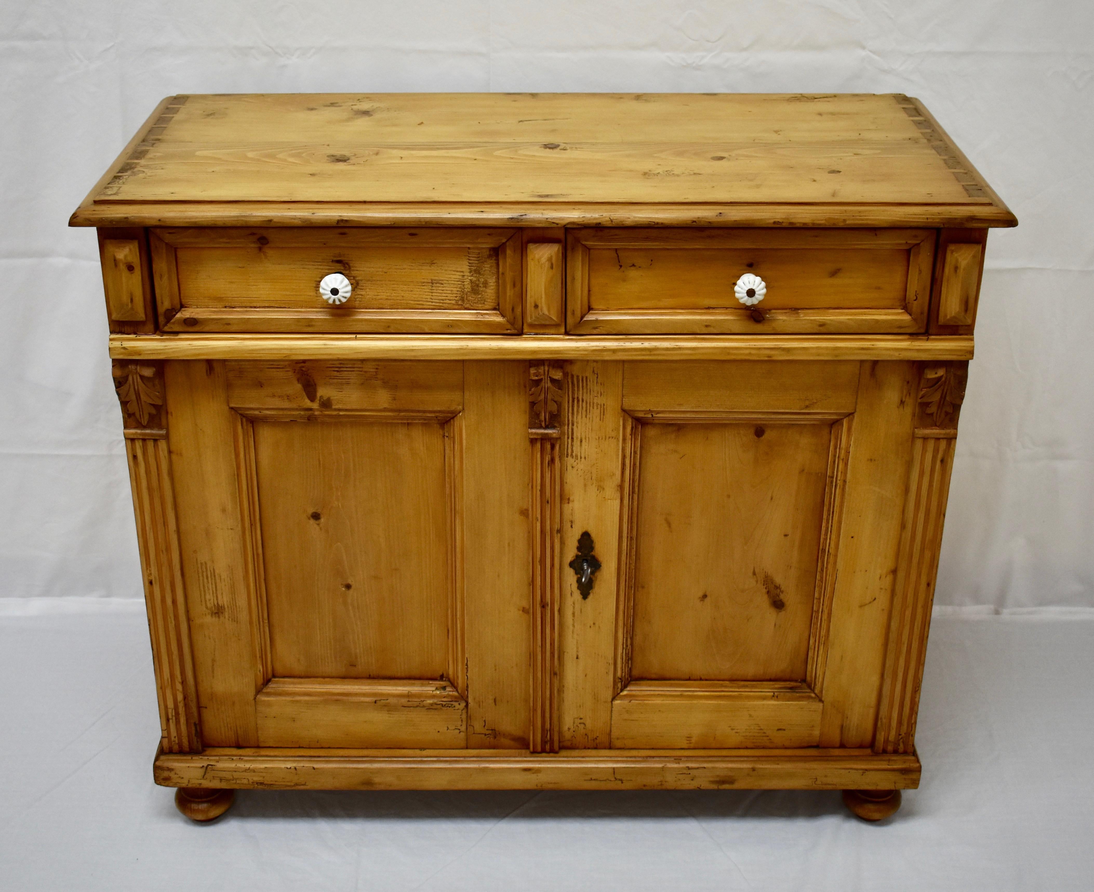 This is an extremely attractive and versatile two door, two drawer pine dresser base. The top shows half-exposed dovetails bordered by a step-down applied molding.
Two lap-jointed drawers with ceramic knobs sit above two flat-paneled doors, flanked