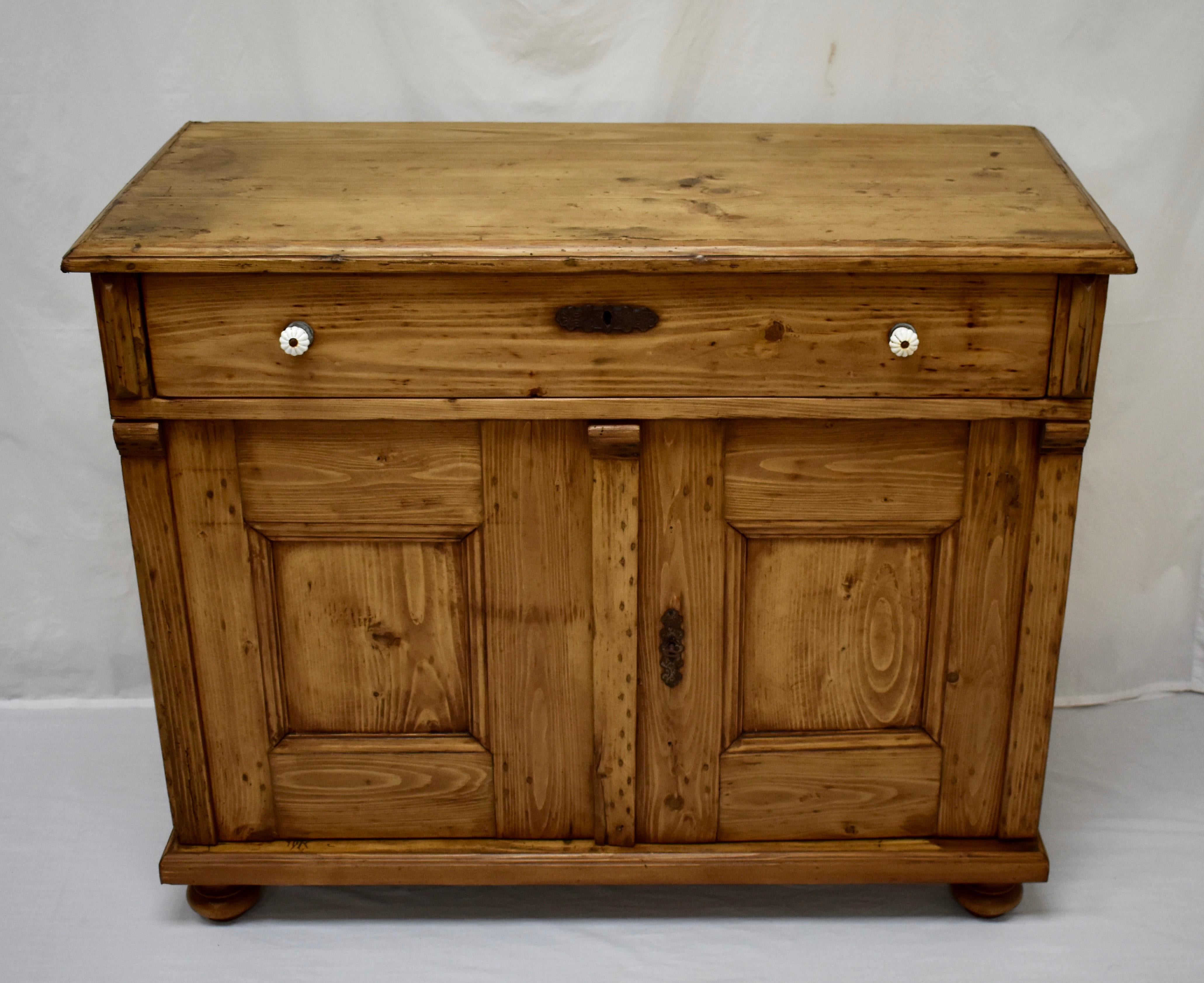 This is a fairly plain pine two-door dresser base with lots of character. The two board top, scratched and stained with small patches of filler and a few small candle burns, is banded with an applied molding and sits above a single long handcut