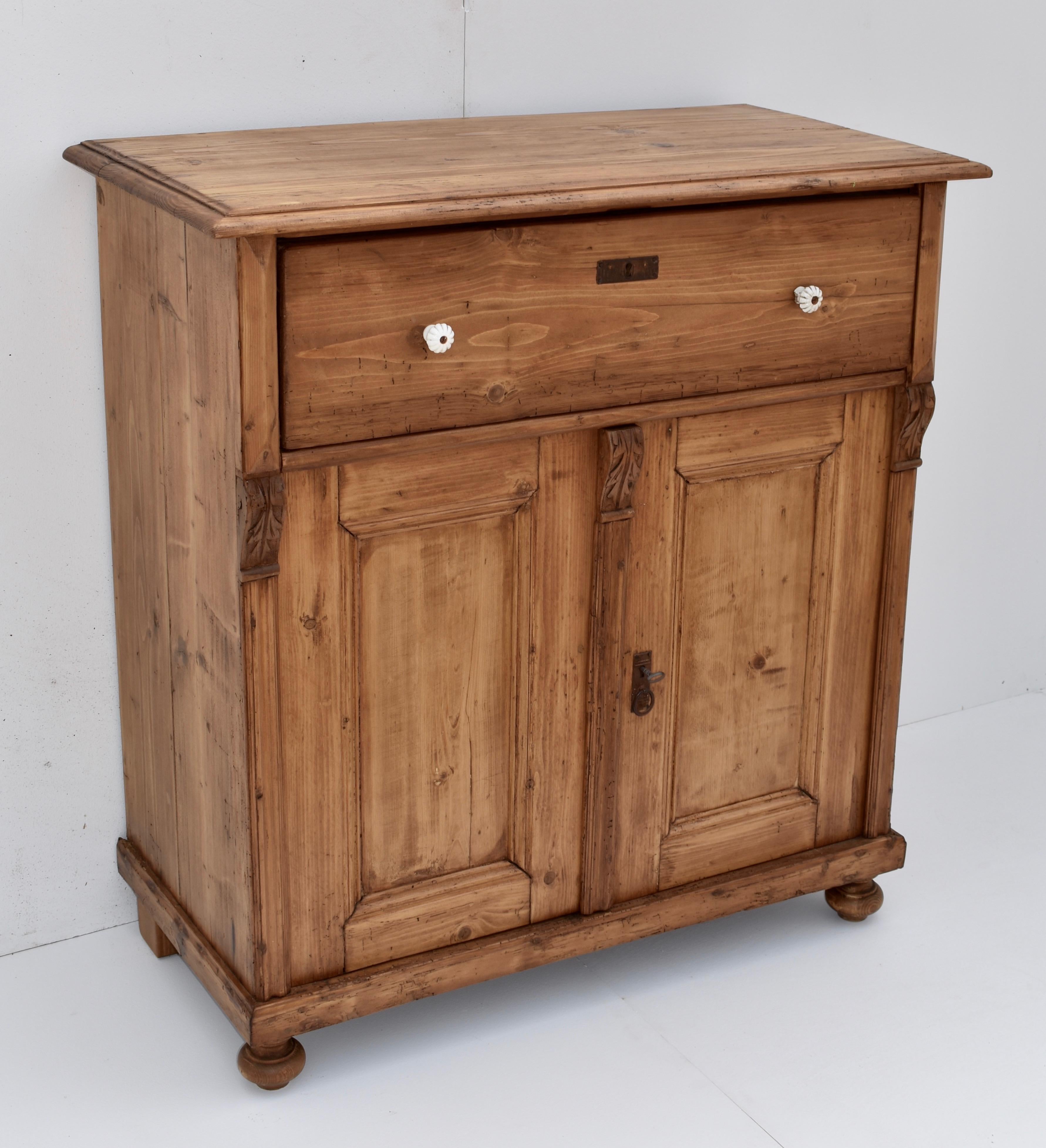 This useful pine dresser base has a step-down top edge, a single deep drawer and two flat-paneled doors with bold frames. The front corners are fluted with carved hardwood acanthus leaf corbels.