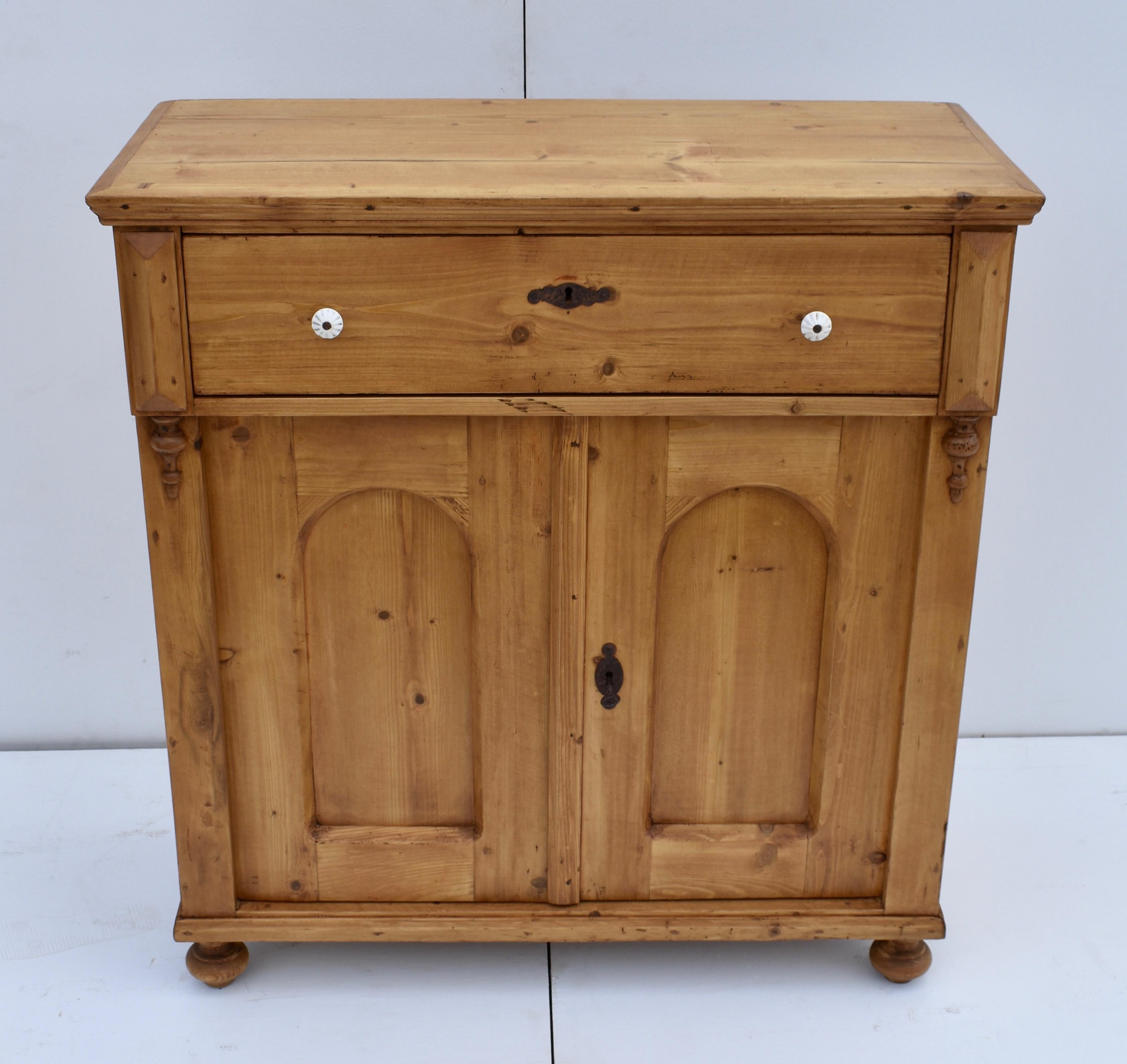 This is a pretty little pine two door dresser base with a versatile shallow profile. The top is trimmed with an ogee molding and sits above a single hand-cut dovetailed drawer with original ceramic knobs. The arched-paneled doors open over ninety