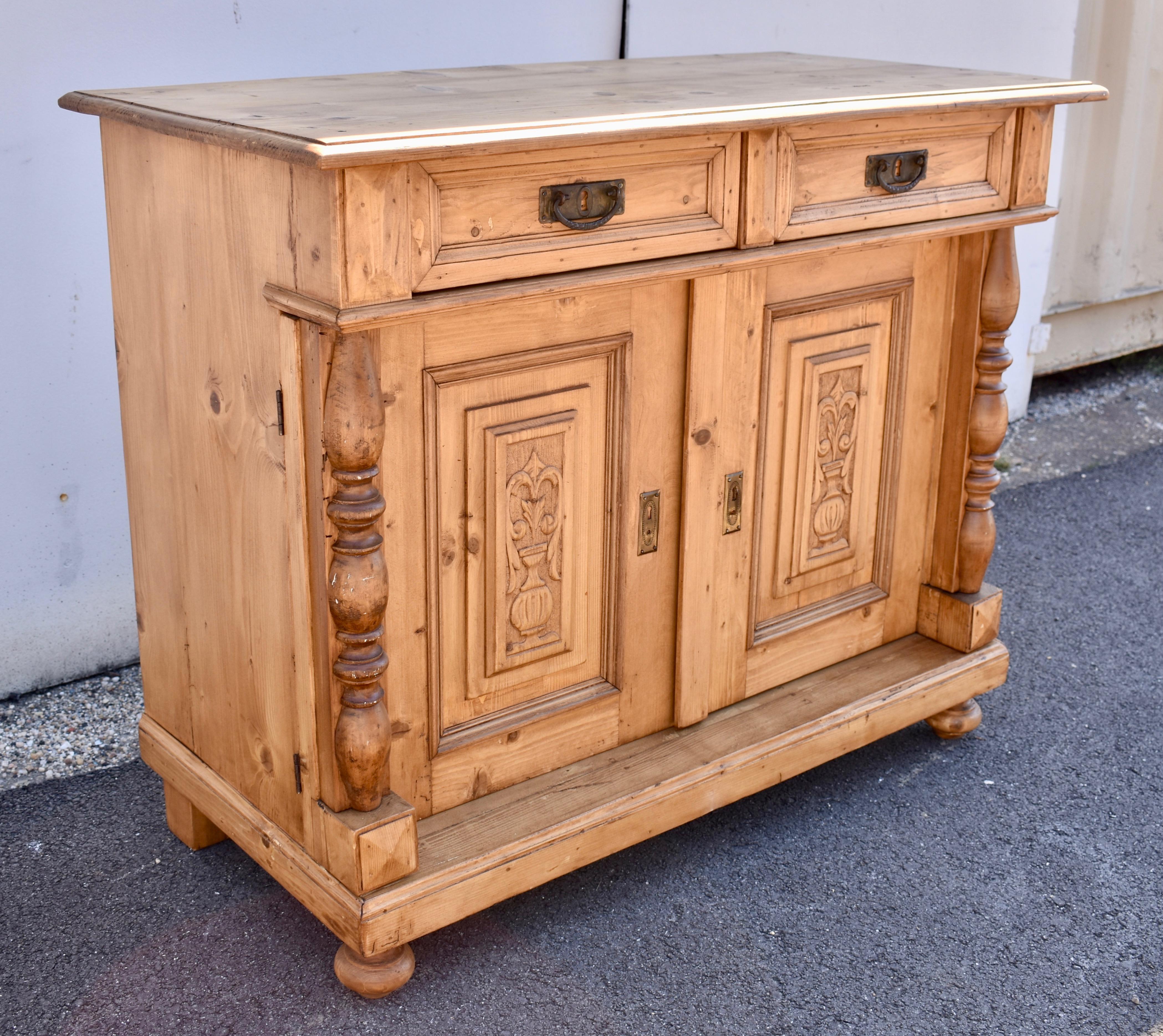 This handsome dresser base has a step-down edge to the top over two dovetailed drawers which stand proud of the front of the piece.  Two doors have raised panels featuring stylized carved urns bearing flowers.  These are flanked by hardwood split