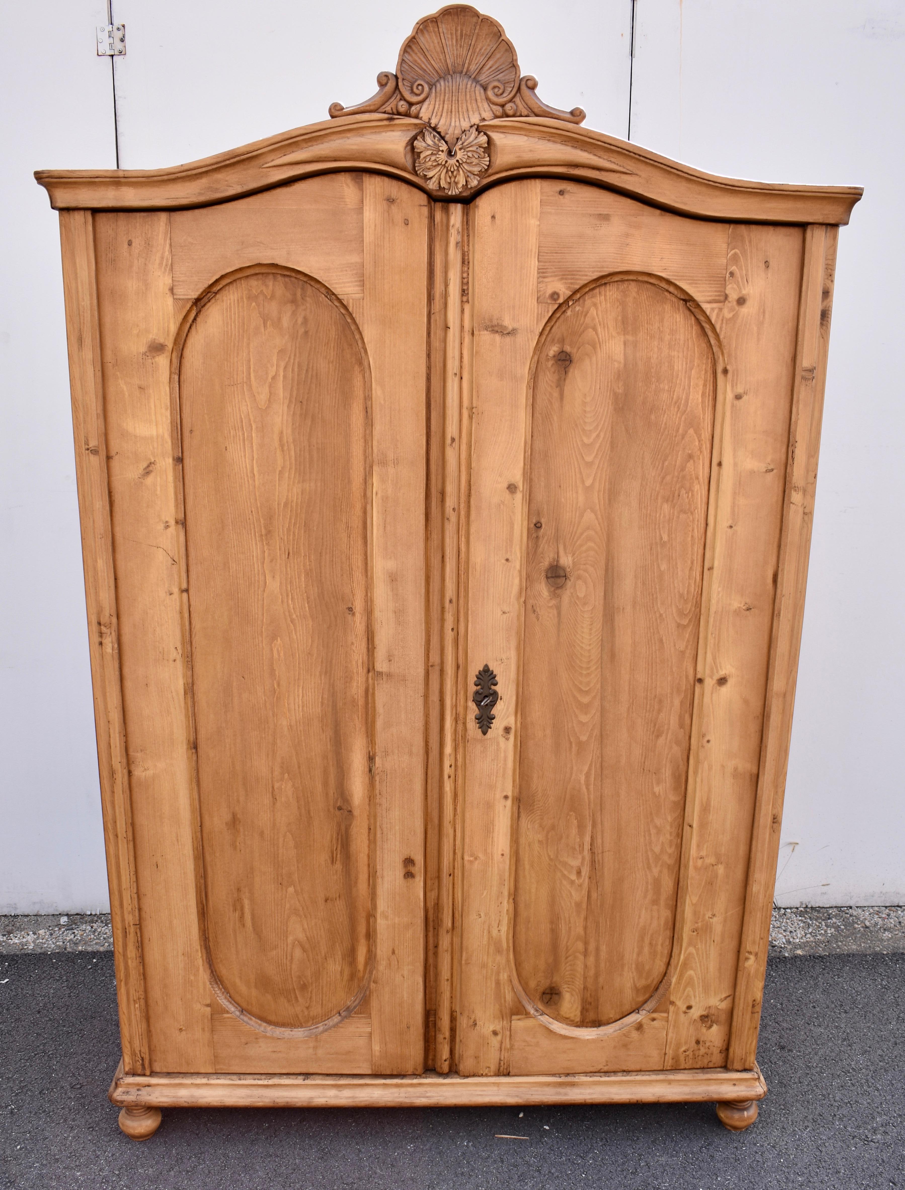 This interesting two door armoire has a serpentine crown molding with a carved hardwood floral medallion in the center and a shell motif crest perched above.  The doors are arched, following the lower line of the crown, and each one has a single