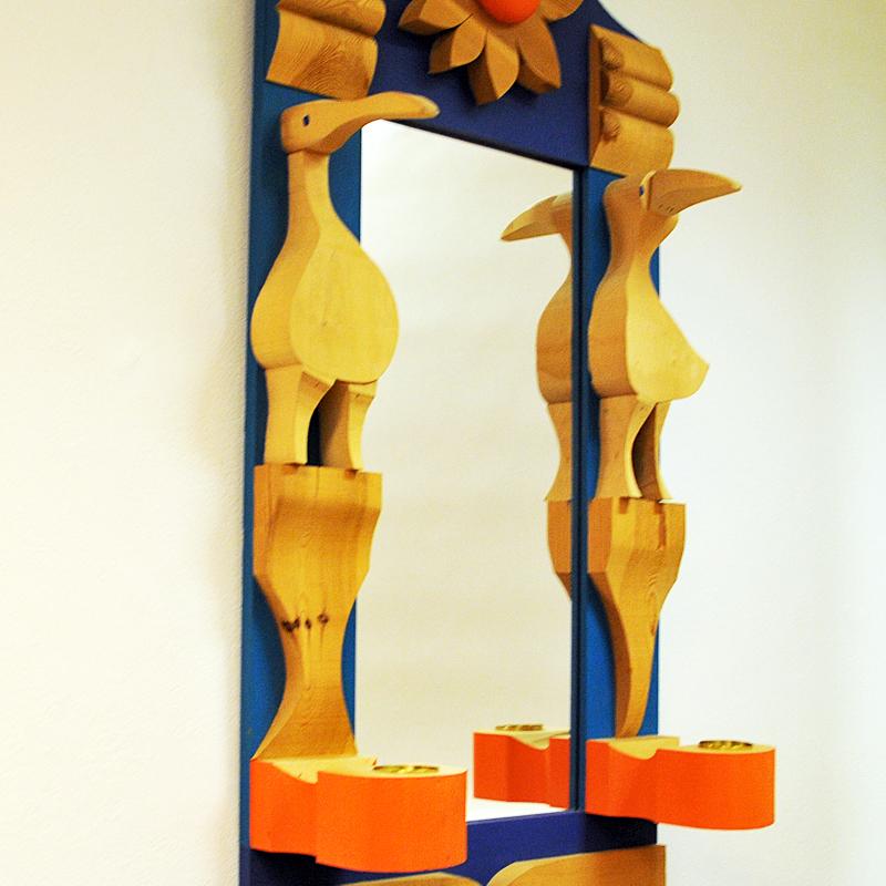 Magnificent and stunning pine wall mirror designed by Erik Höglund for Eriksmålaglas in the 1960s Sweden. Carved and paintet wooden figurines as birds, sun and candleholders in a beautiful mix of blue, light blue, orange and wood colors.
This