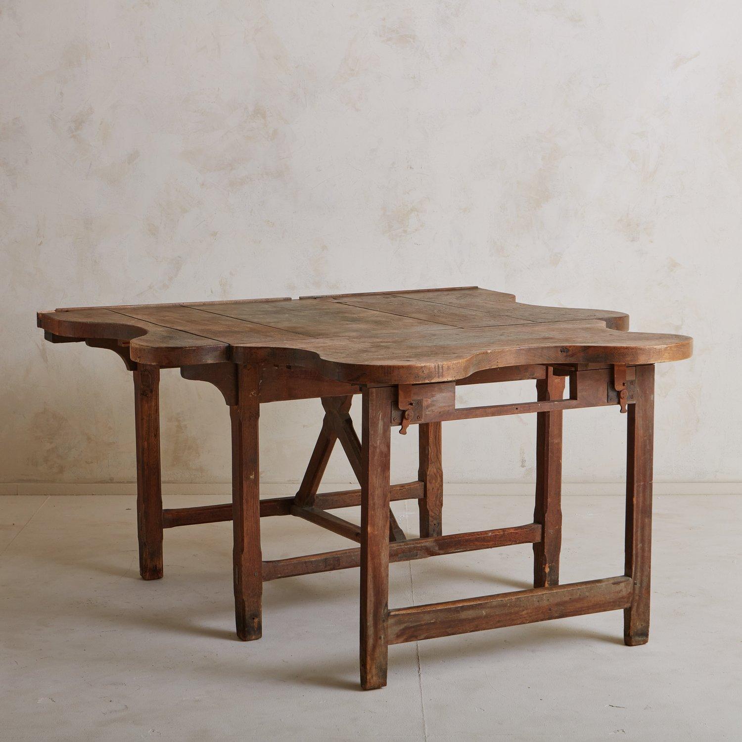 An antique pine wood table sourced in France. This unique piece has one leaf with curved edges and features a stunning patina. The leaf attaches to the sides of the table with pegs and stands on hinged wooden supports, making it easily collapsible