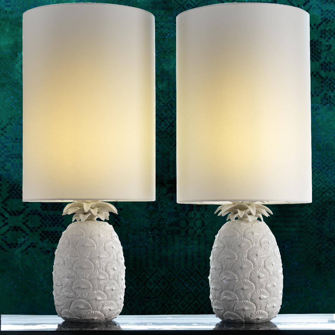 This unconventional table lamp strikes with the minute details inlaid on its porcelain base. Its structure includes a bold, cylindrical lampshade that hosts a single lightbulb supported by a porcelain base shaped like a pineapple depicted in