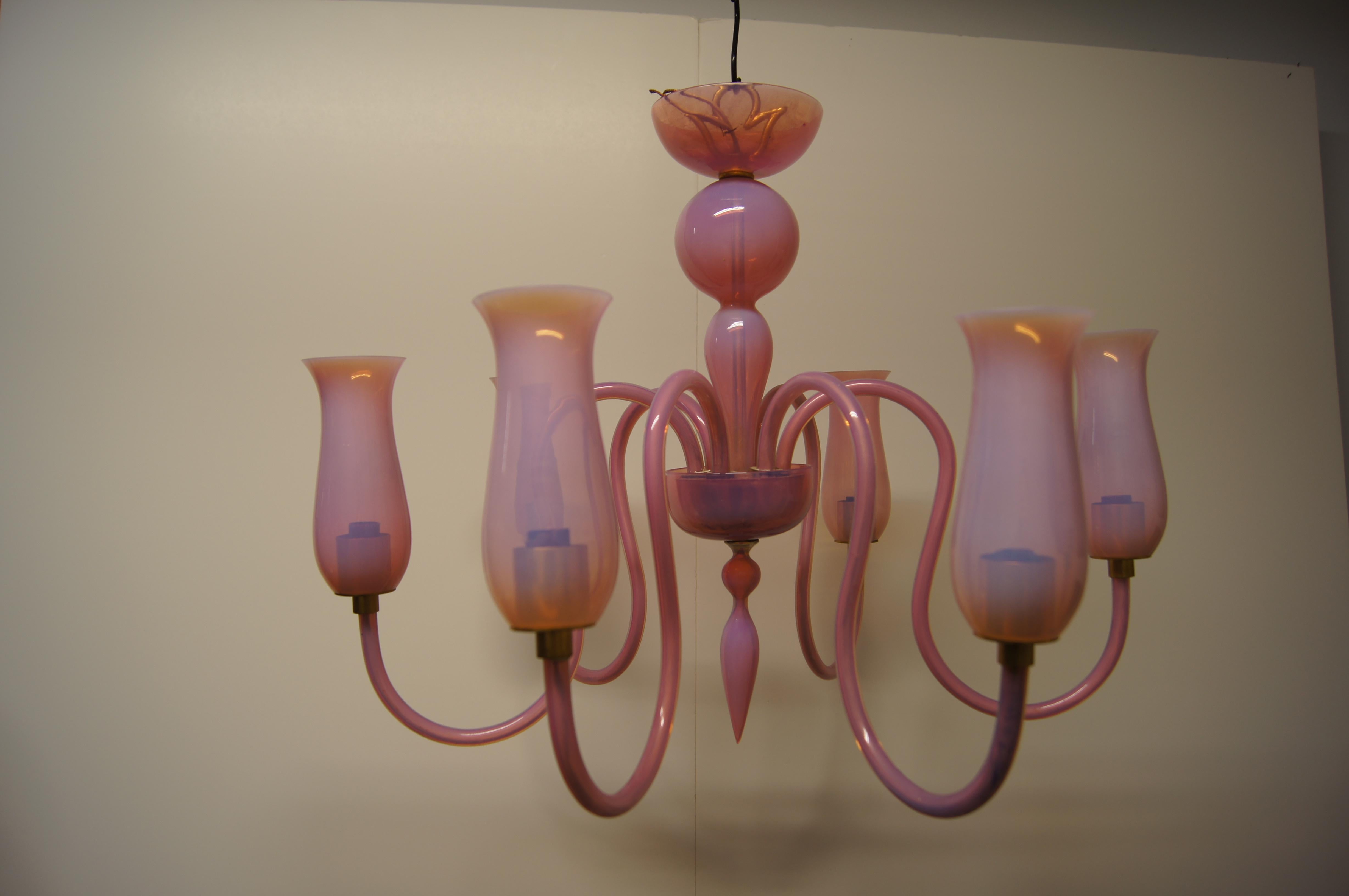 This lovely chandelier of pink Murano glass was created in 1950s Venice. Radiating in undulations from a central stack of varied blown-glass shapes, six glass arms end in tall blown-glass vessels set over the lamps.