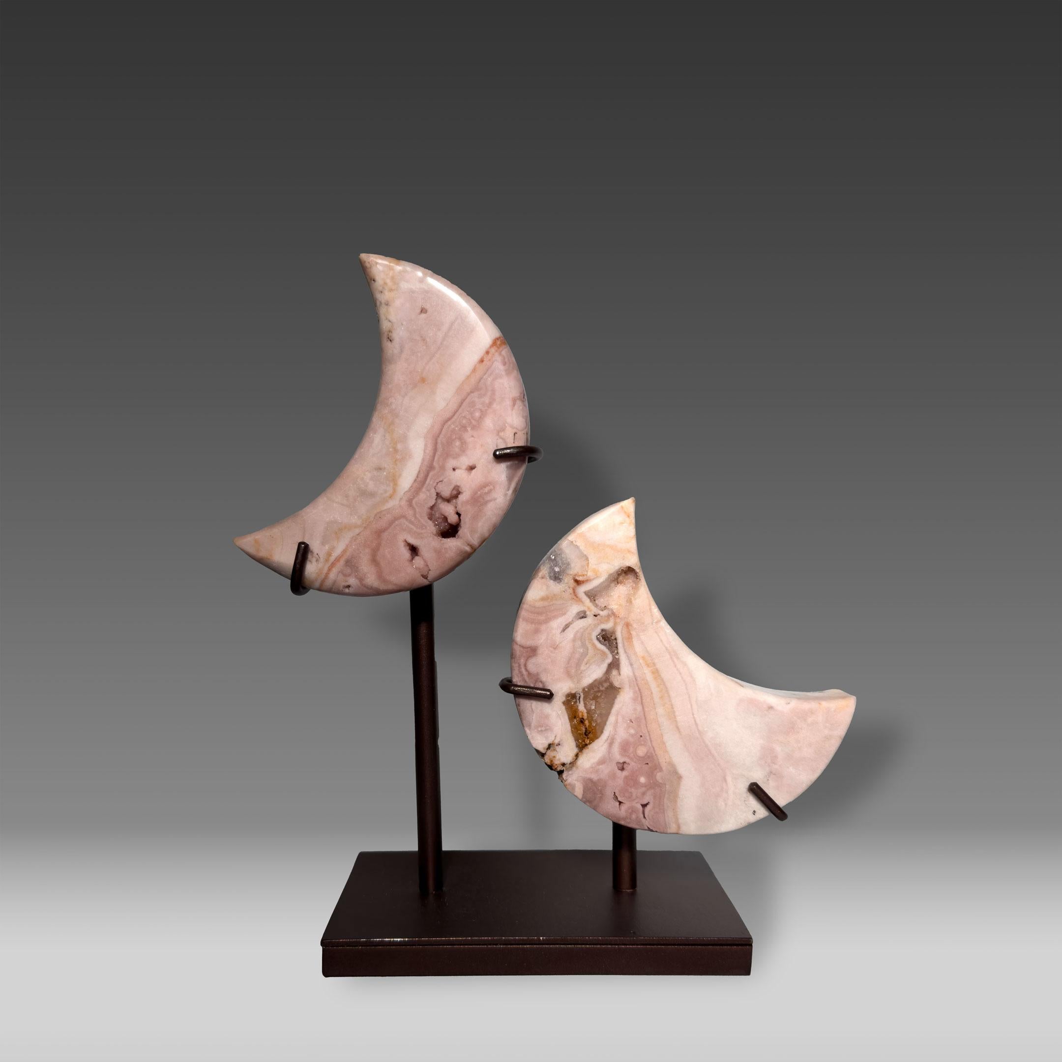 This striking pair of hand-carved Pink Amethyst crescent moons is mounted on a custom metal stand, creating a sculptural display that blends elegance with natural wonder. The soft blush and lavender tones, accented by delicate banding and subtle