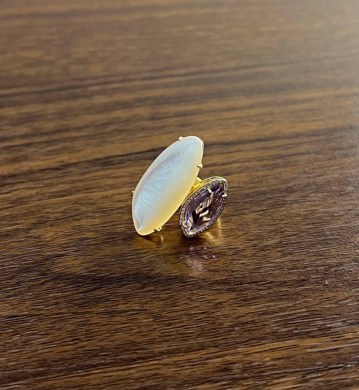 Cette bague exquise présente un design frappant avec deux pierres distinctes. L'une des pierres est une nacre blanche lumineuse et allongée, aux reflets irisés captivants. L'autre est une pierre précieuse facettée d'une délicate teinte