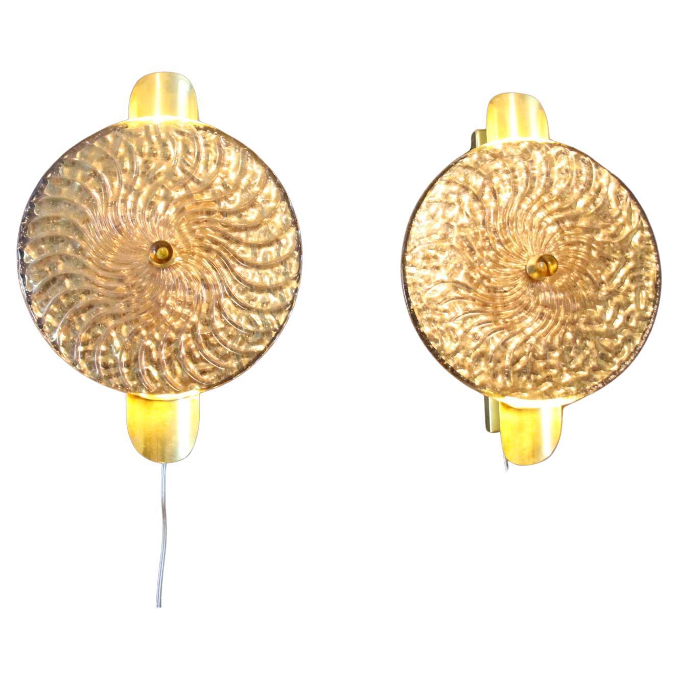 This striking pair of wall lamps is made of textured pink Murano glass disk worked like a spiral swirled, put on a textured brass plate to produce this exceptional effect of changing color between pink and gold . This work of art reaches a high