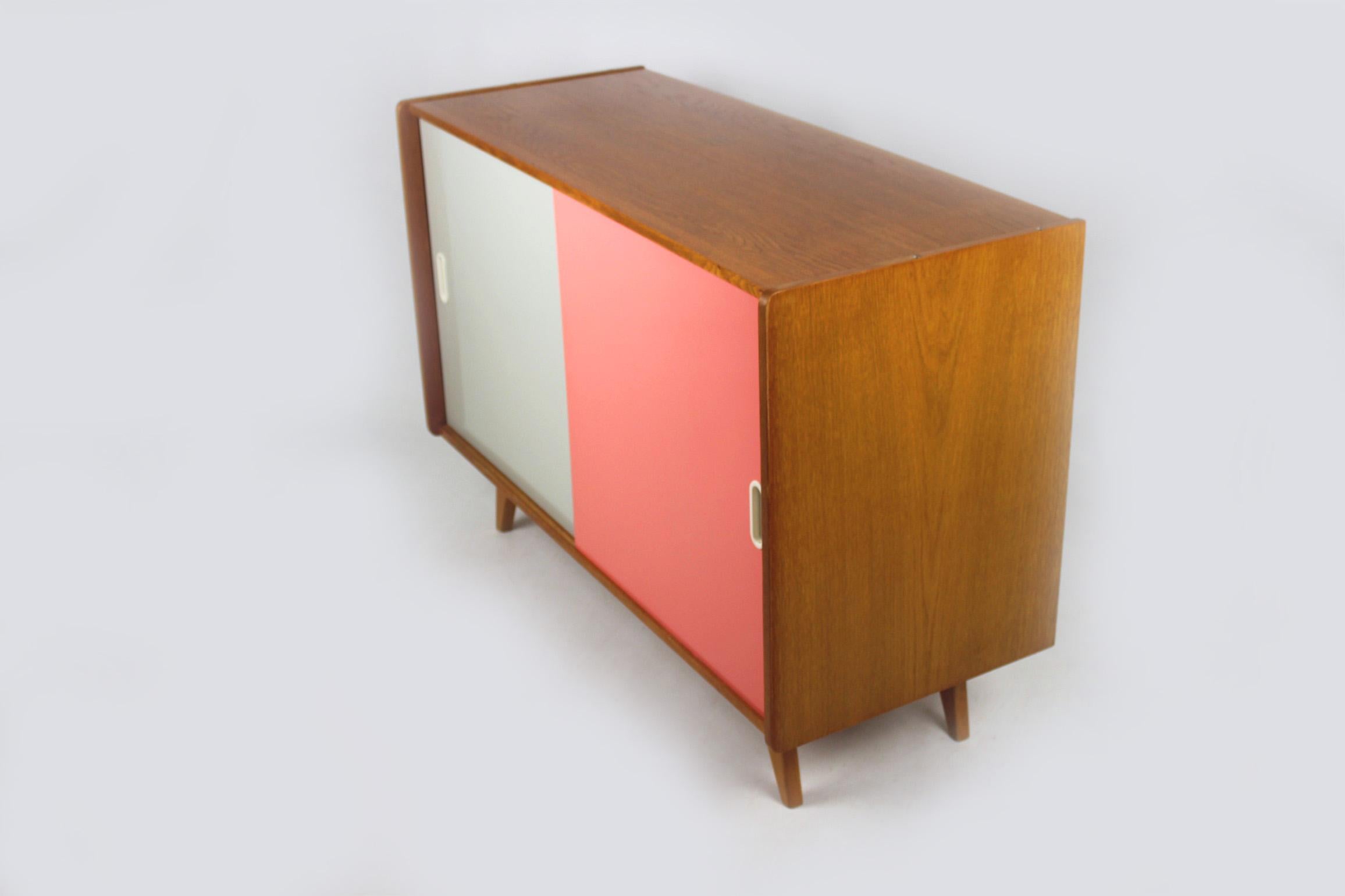 This midcentury wooden sideboard with slide doors was designed by Jirí Jiroutek for Interiér Praha in the 1960s.
Features one long shelf inside and original pink and grey formica fronts.