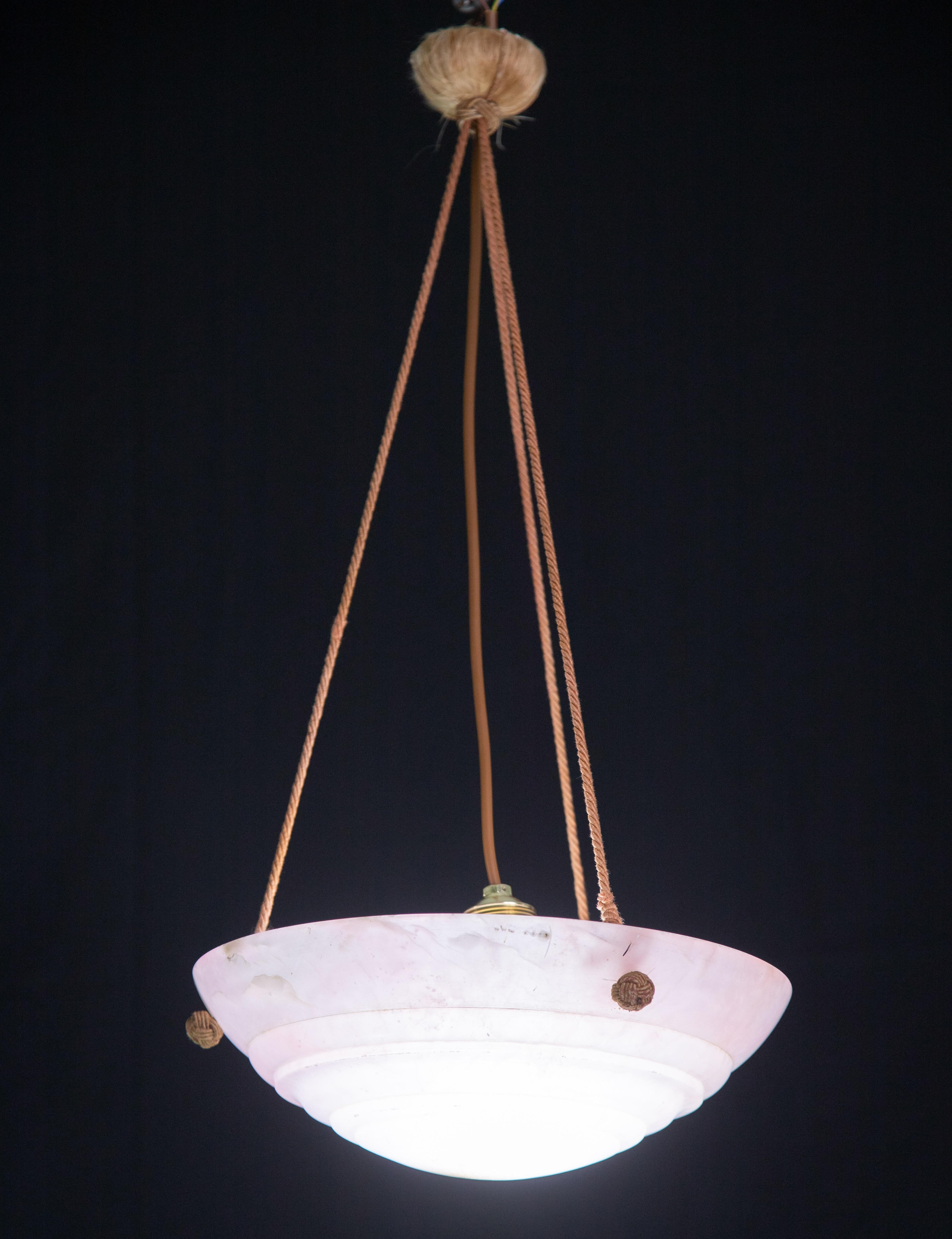 Antique pink alabaster hanging chandelier in Art Deco style, circa 1940s.
A unique piece in pink alabaster, beautifully crafted with hues and reflections of other colors when lit, still suspended from the three original chains.
The light that shines