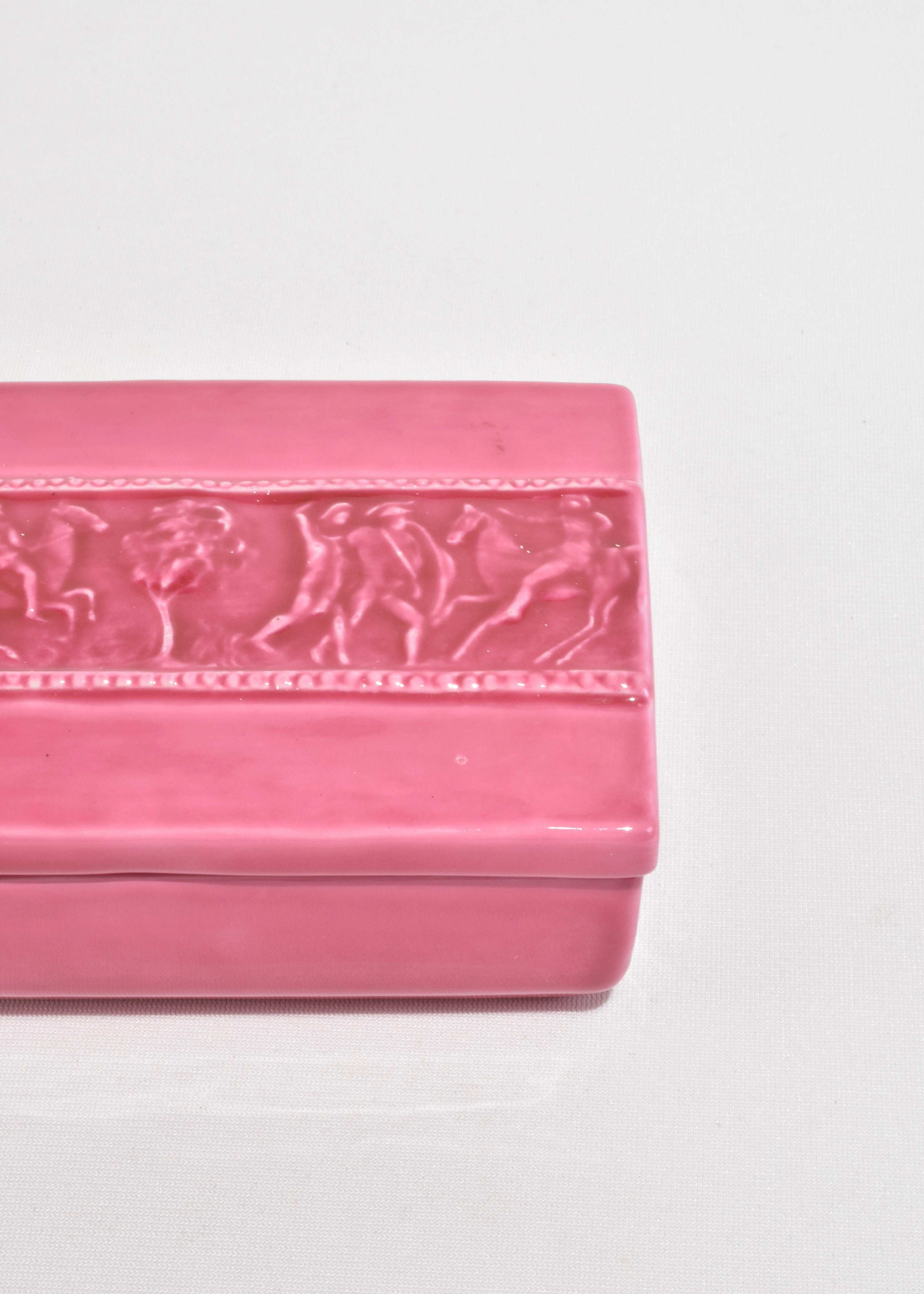 Caja rectangular vintage de cerámica con esmalte rosa intenso brillante. La tapa presenta una banda en relieve que representa una escena clásica con caballos y figuras. Estampado en la base, Italia.