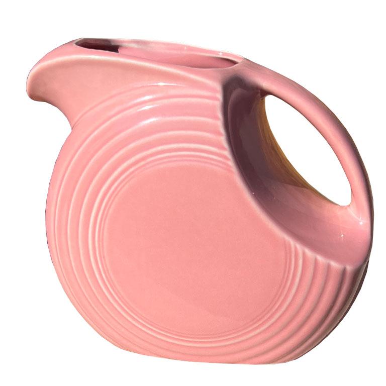 A classic Fiesta ware disc pitcher in the discontinued color Rose. Highly collectible, Fiestaware has been a favorite among collectors for ages. This glazed pink ceramic pitcher is disc shape, and perhaps one of the pieces that Fiesta is most known
