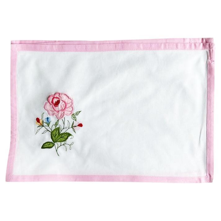 Un juego de cuatro manteles individuales de tela con motivos florales. Cosido a mano, este juego incluye 4 manteles individuales rectangulares en un blanco nítido, con un borde rosa ballet. Cada pieza está decorada con un aplique bordado de una rosa